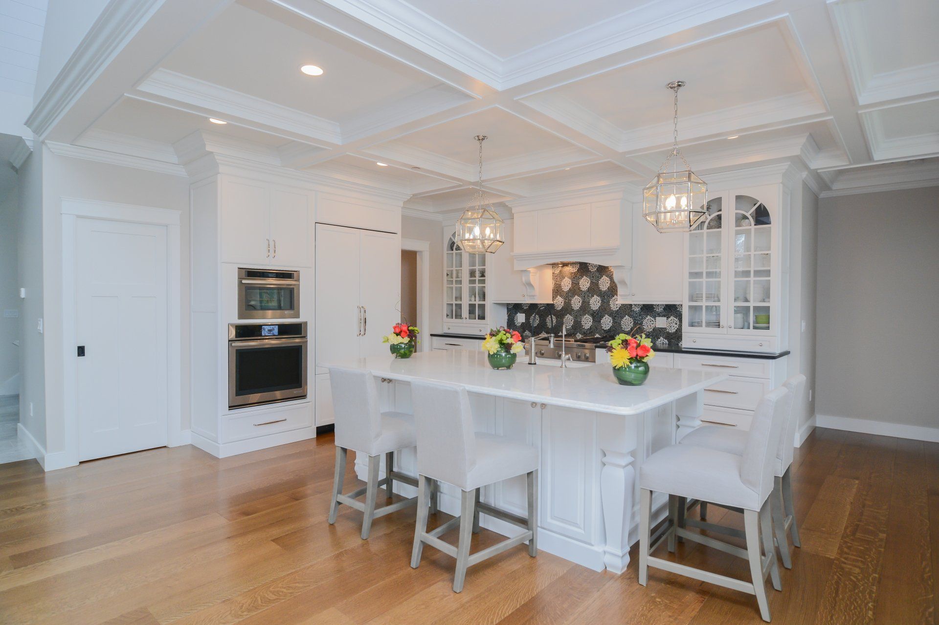 Bright white modern kitchen with marble island, white stools, hardwood floors, and built-in oven