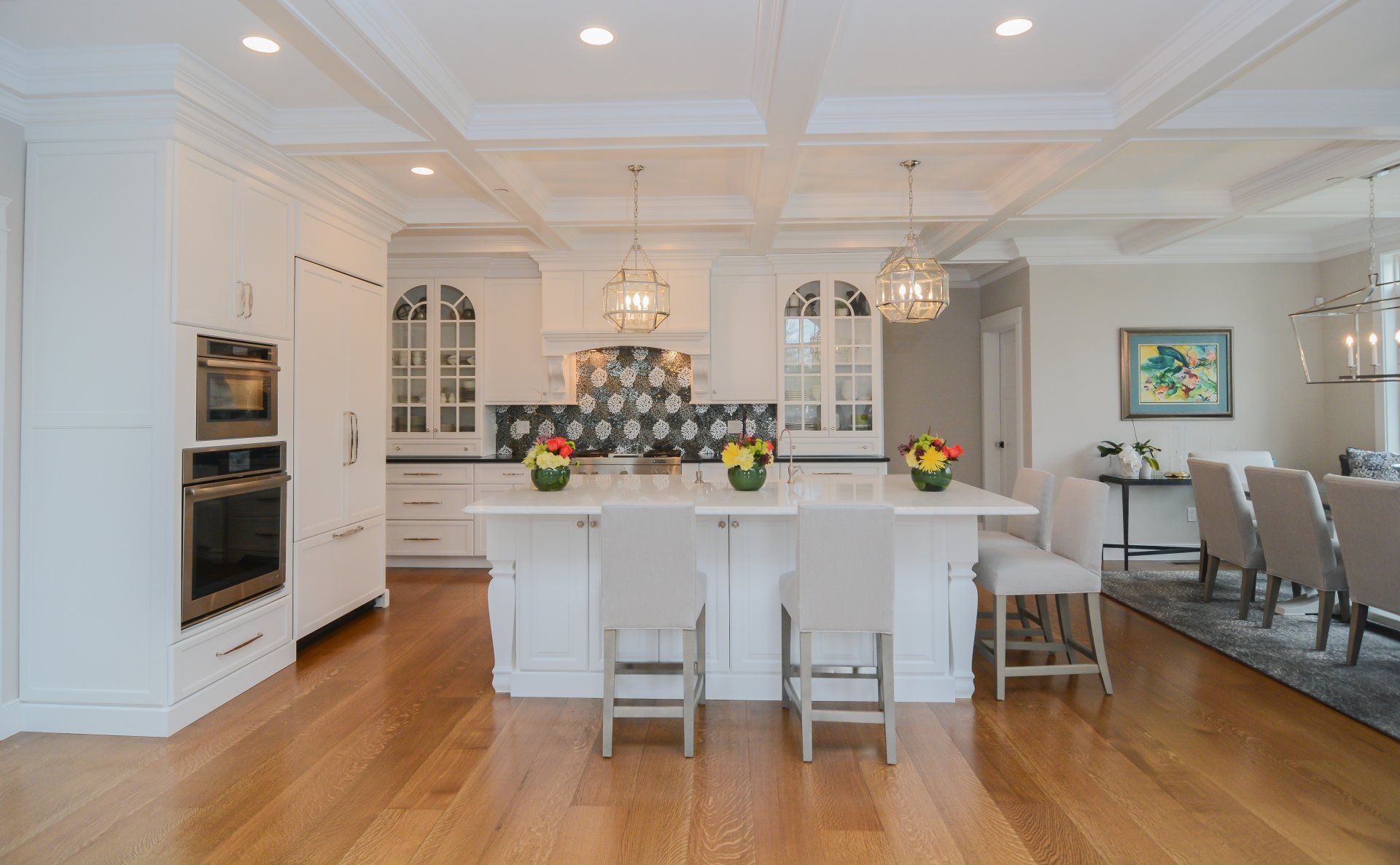 Bright white kitchen with island, pendant lights, hardwood floors, and adjacent dining area