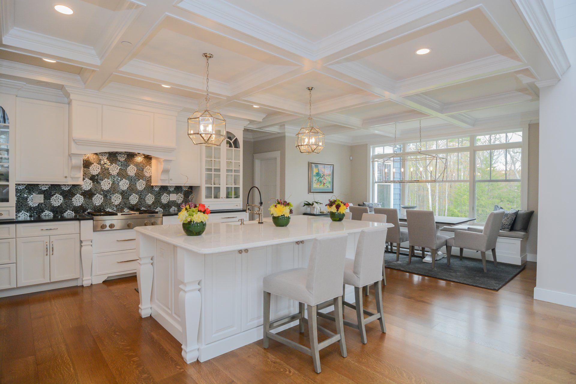 Bright white kitchen with island, pendant lights, wood floors, and cozy seating area by windows