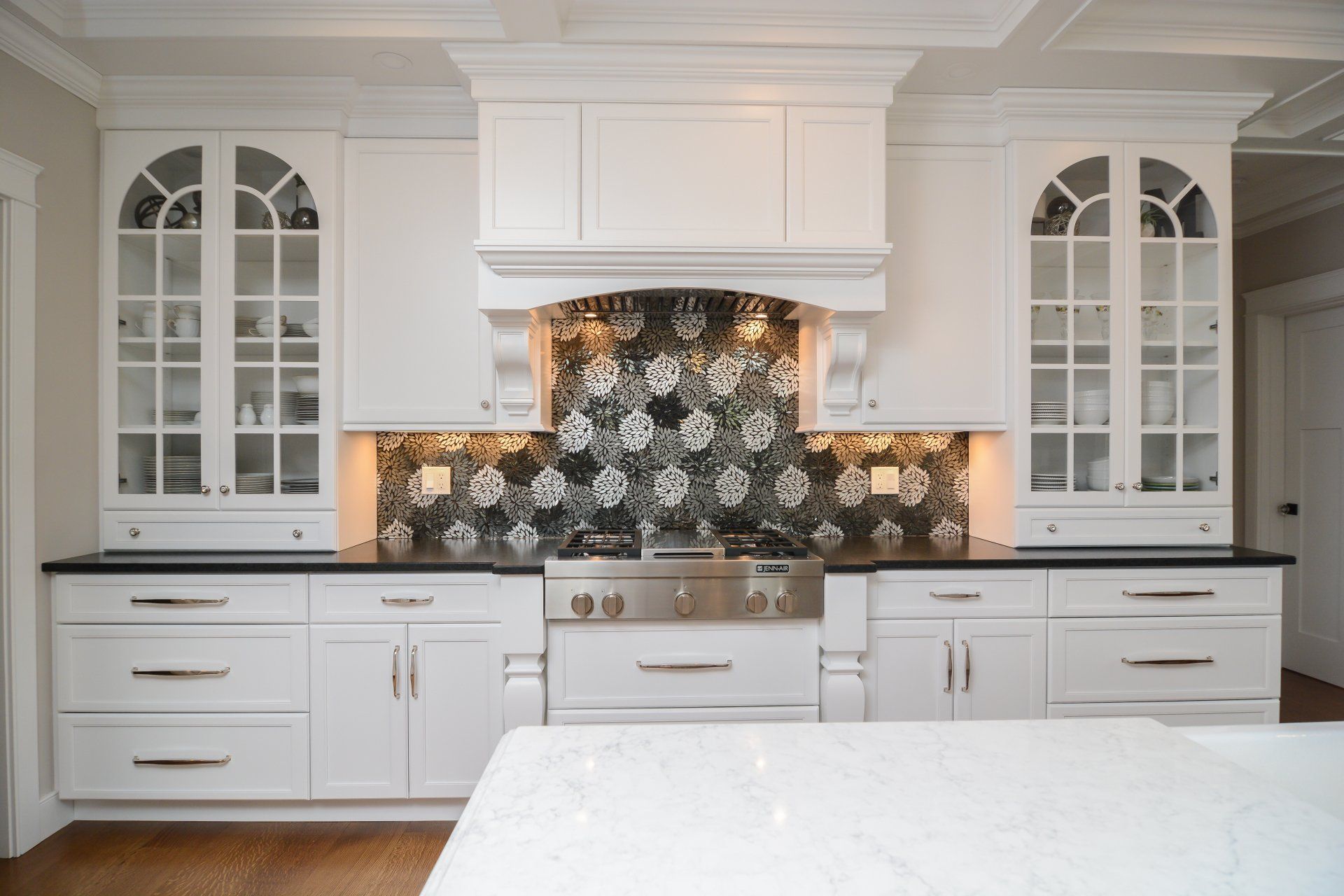 White kitchen with patterned tile backsplash, stainless stove, and glass-front cabinets