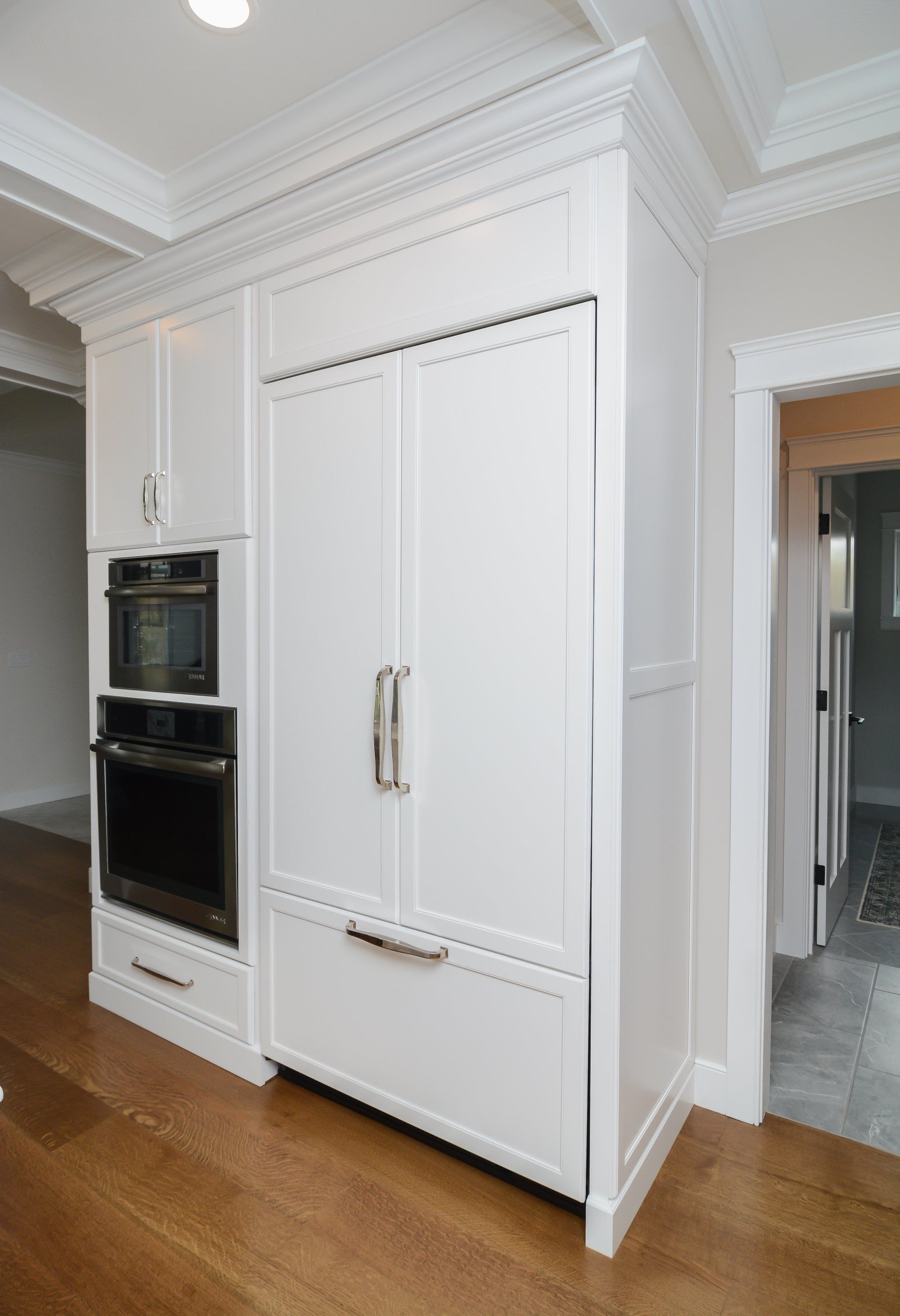 White built-in kitchen wall with double oven and refrigerator drawers in a bright modern interior