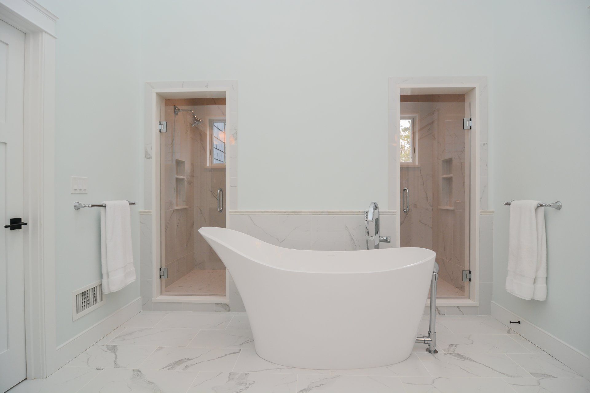 Bright white bathroom with a freestanding tub centered between two open doorways and wall towels.