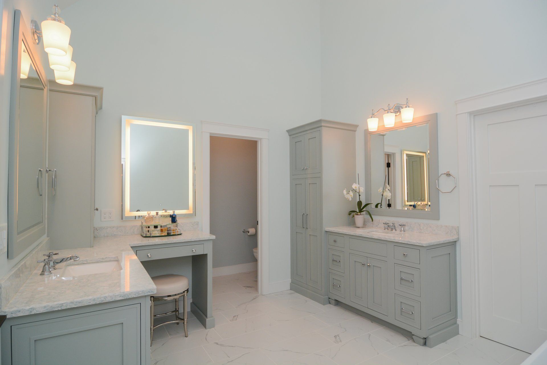 Bright bathroom with two vanities, large mirrors, white tile, and a closed door.
