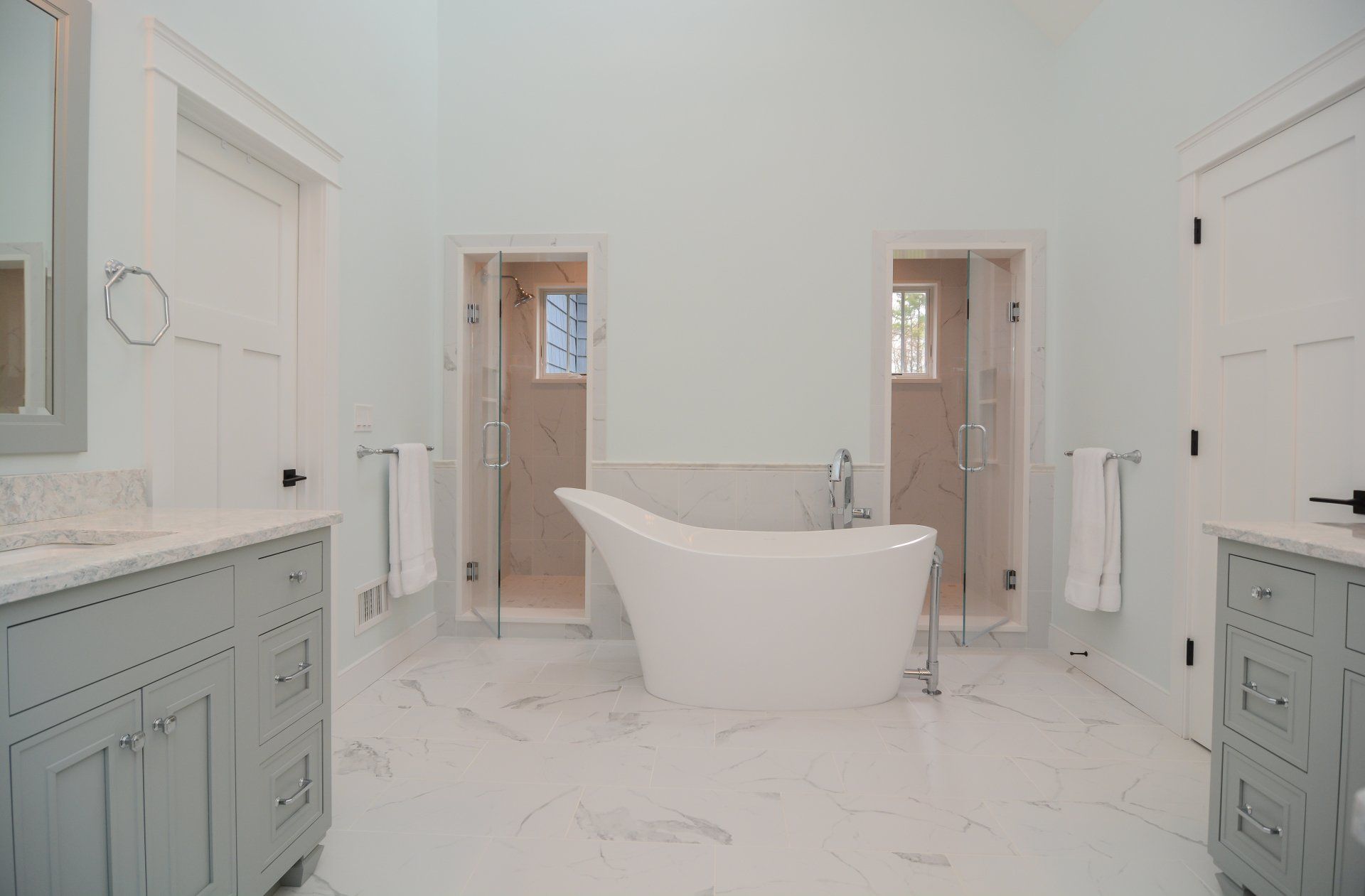 Bright marble bathroom with a freestanding tub, double vanities, and two shower stalls.
