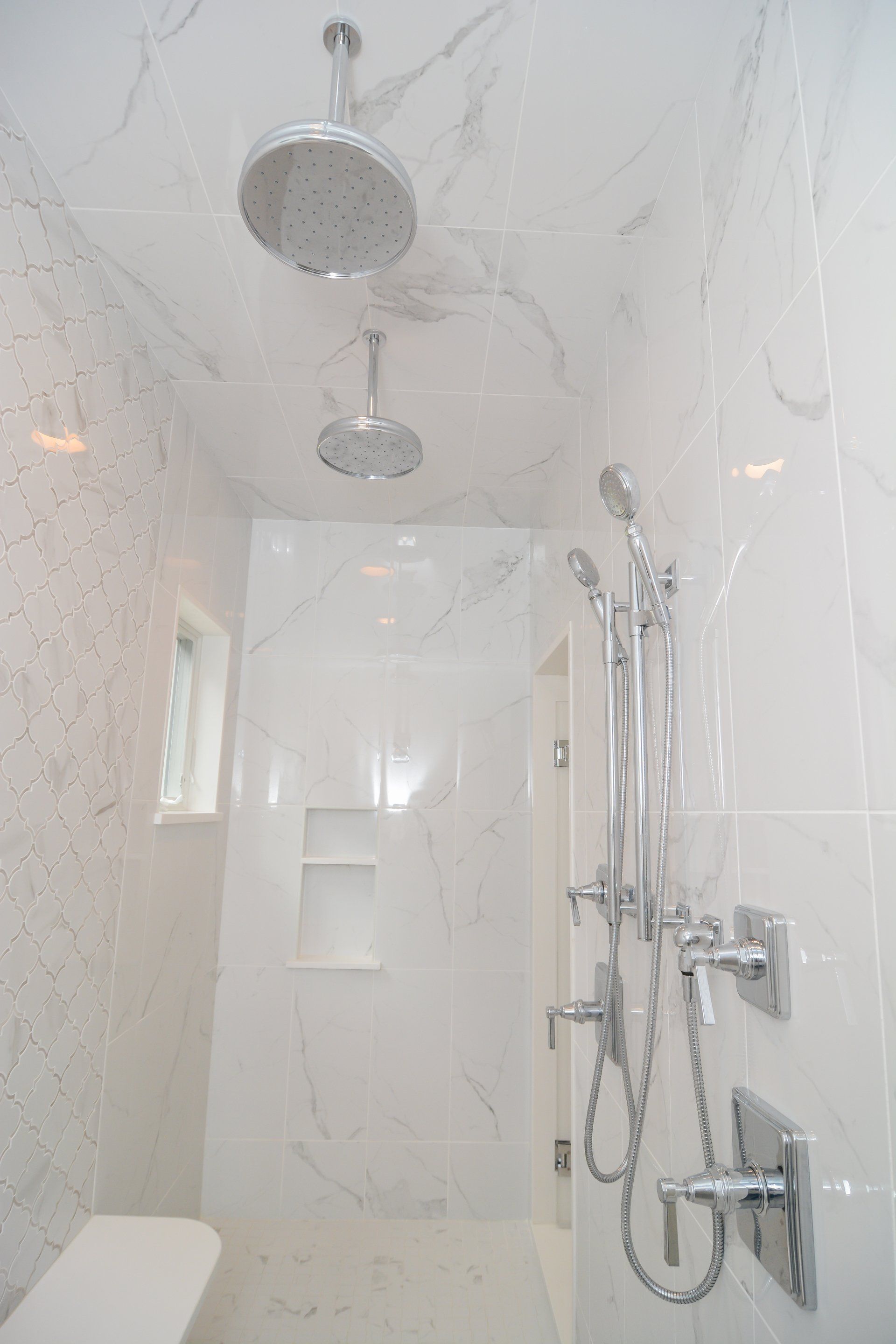 White marble shower with two chrome showerheads and built-in wall niche.