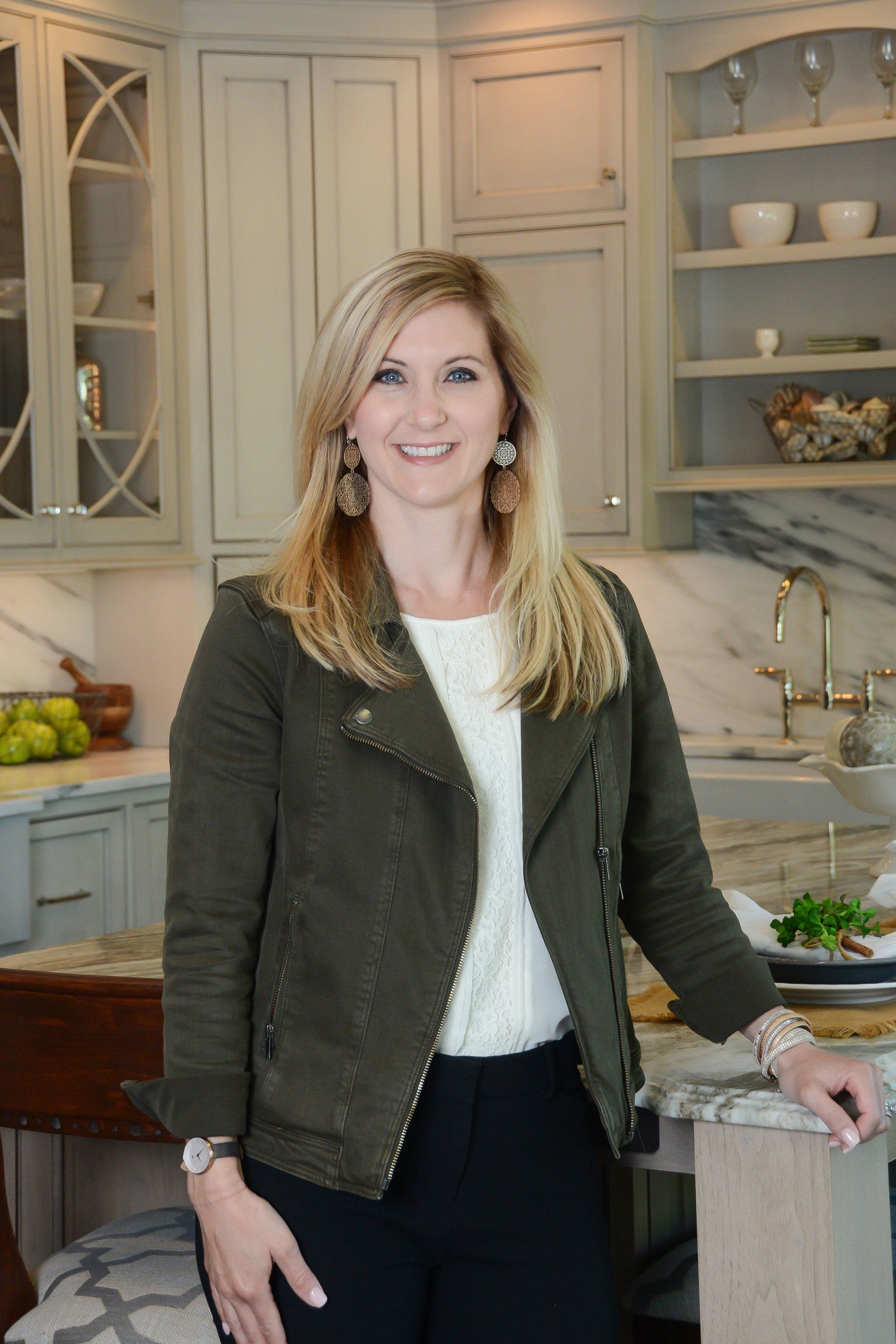Woman standing in a bright kitchen with light cabinets, a marble island, and a bowl of fruit.