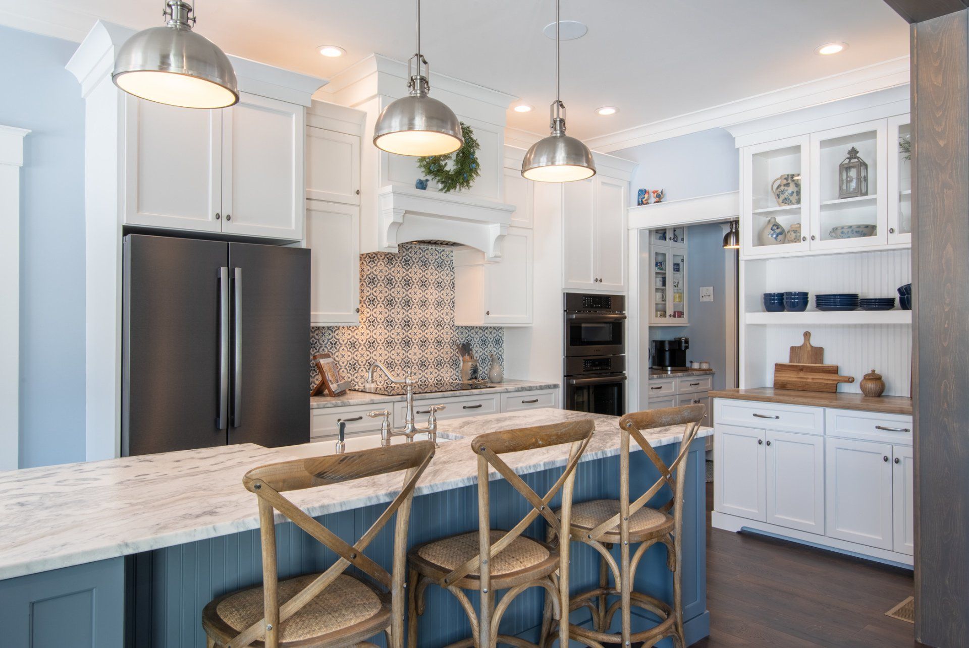 Bright modern kitchen with white cabinets, stainless fridge, island with blue stools, and pendant lights