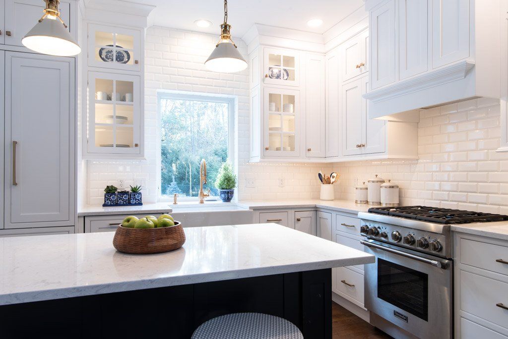 Bright white modern kitchen with island, pendant lights, stainless stove, and window over the sink