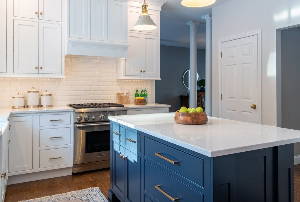 Bright white kitchen with blue island, stainless stove, and pendant lights