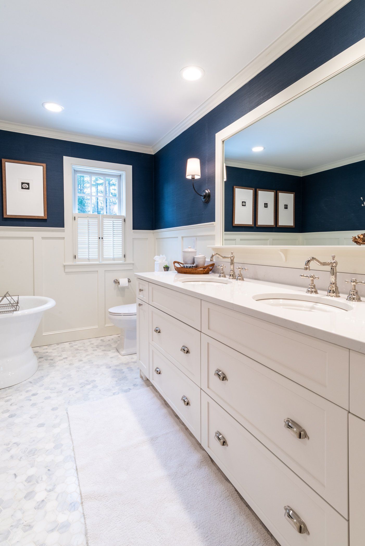 Bright bathroom with white vanity, dark blue walls, large mirror, and a bathtub by a window