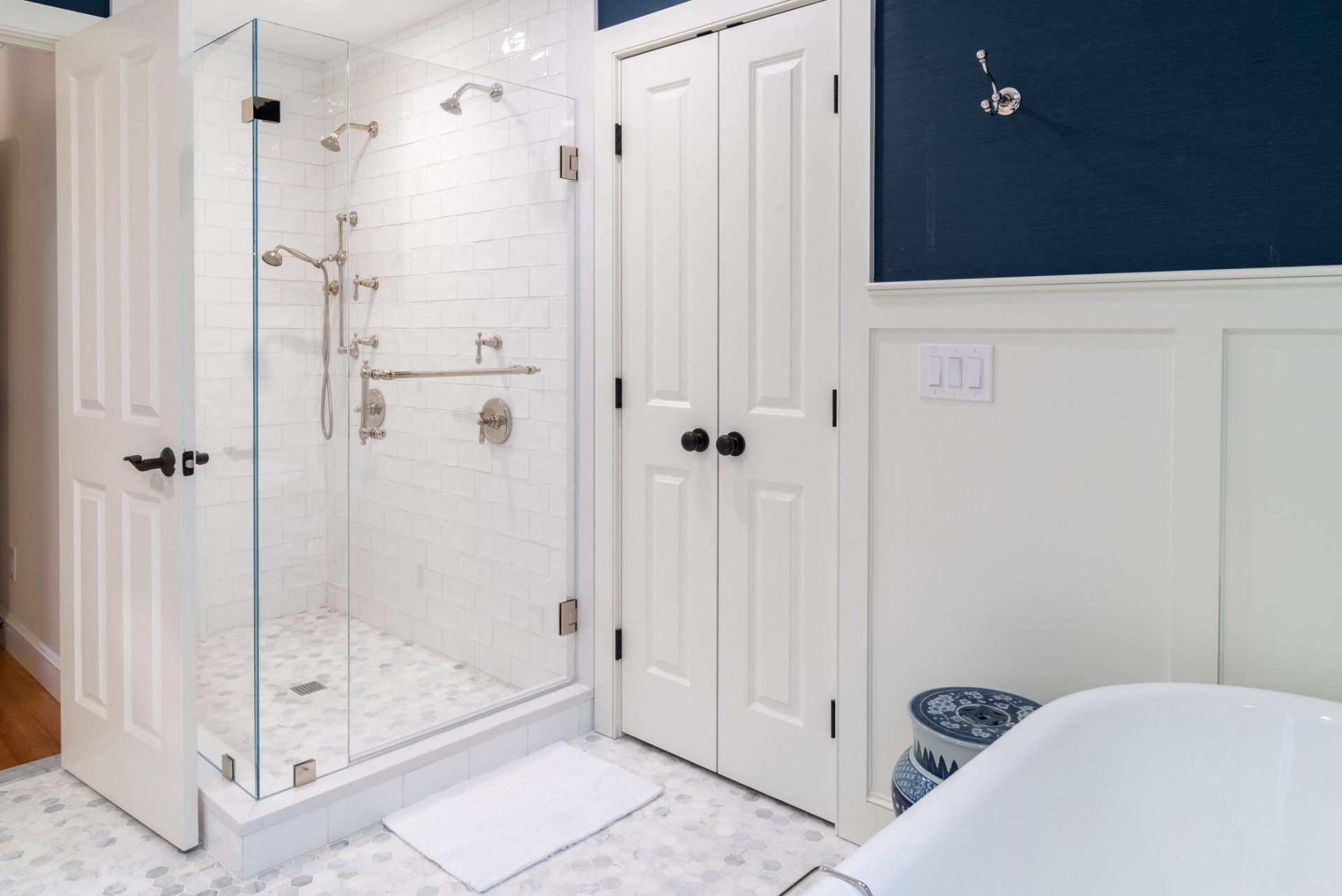 Bright bathroom with glass shower, white tile, and navy accent wall