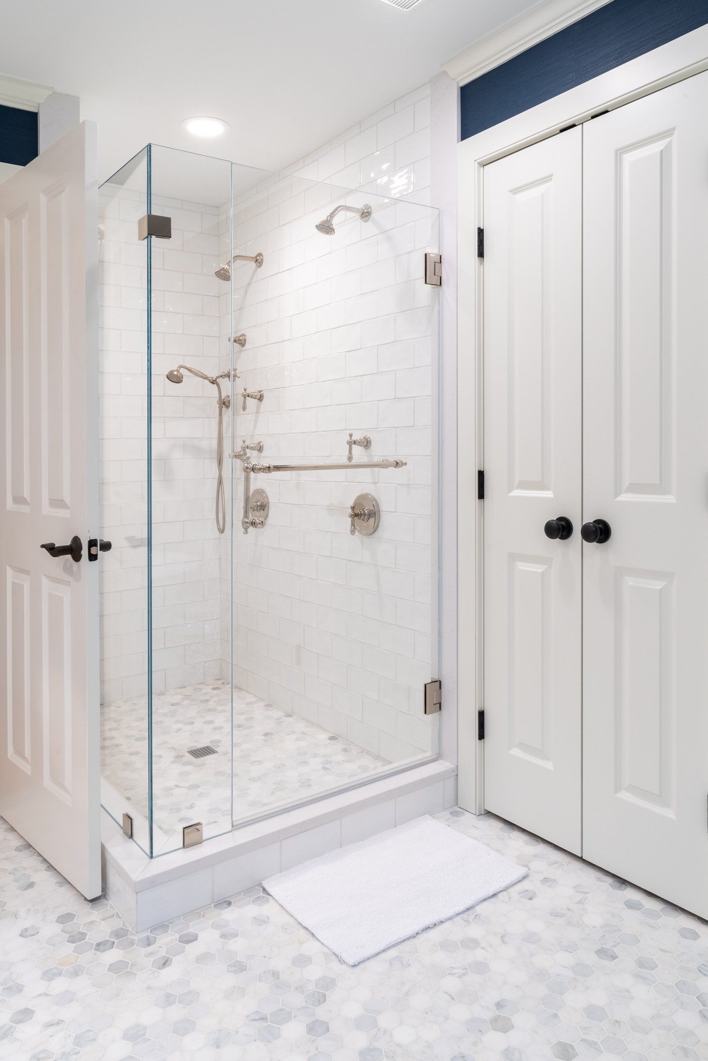 Bright white bathroom with glass shower, marble tile, and double closet doors