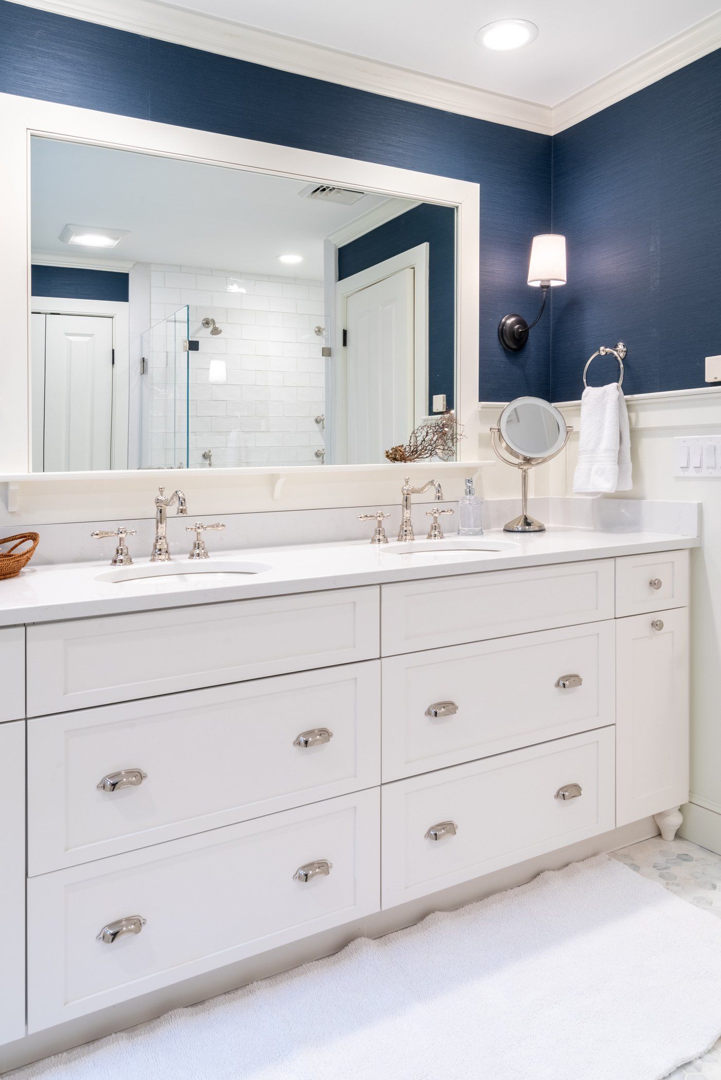 White bathroom vanity with double sinks, large mirror, and navy blue walls, lit by wall sconces