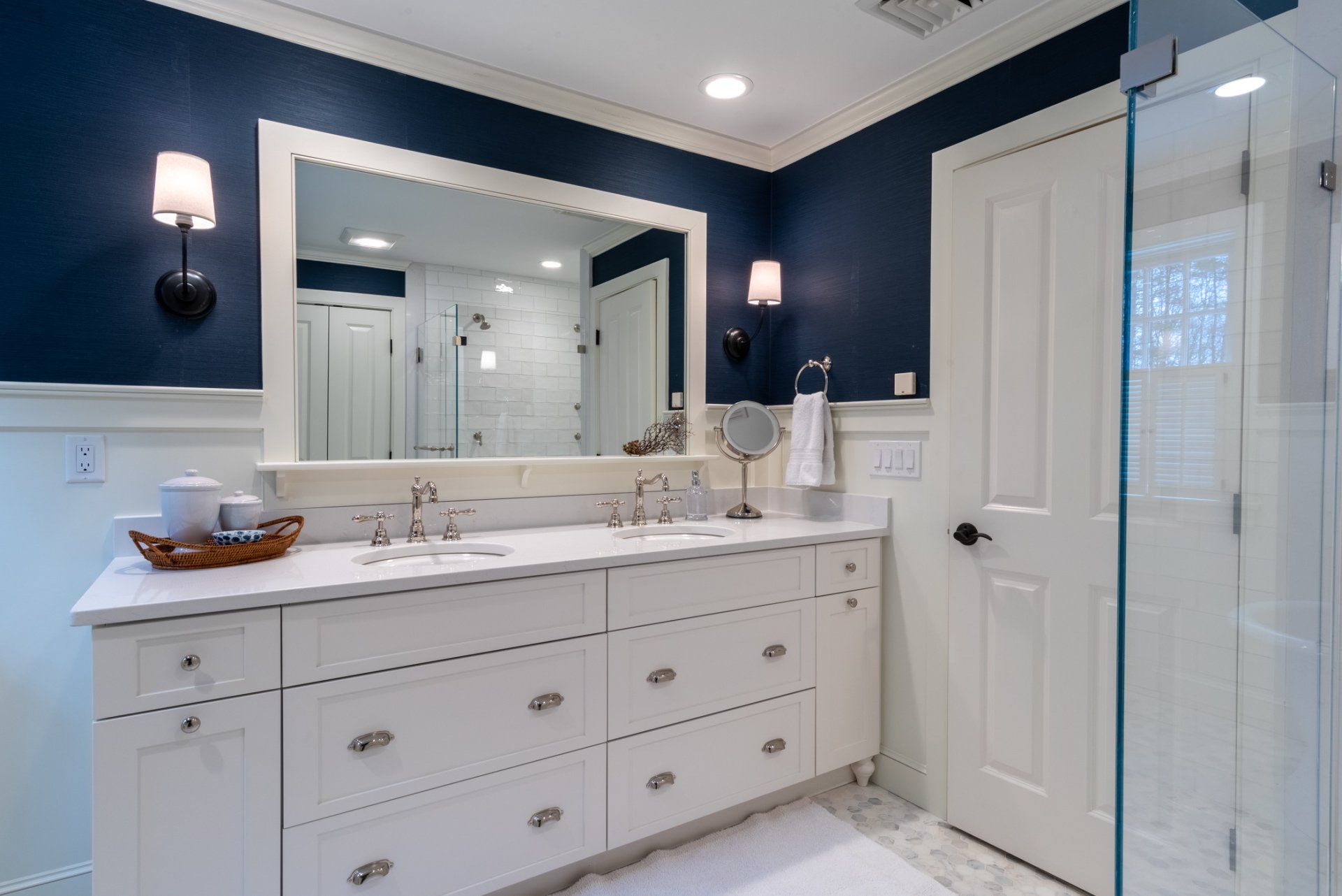 Bright white bathroom with double vanity, large mirror, wall sconces, and glass shower door