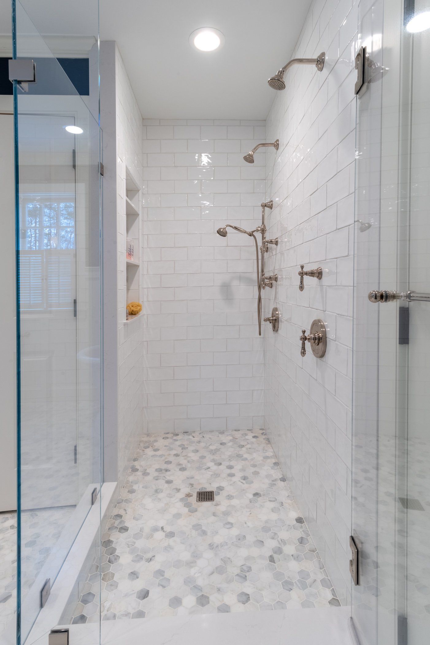 Modern white tiled shower with glass enclosure, multiple chrome fixtures, and pebble-style shower floor.