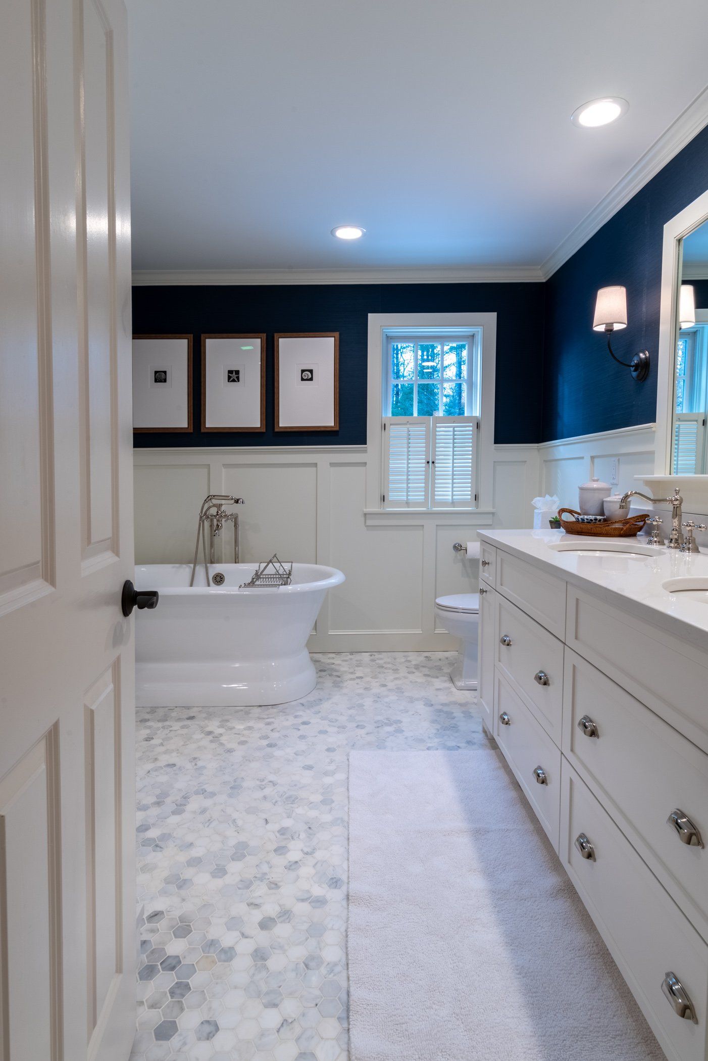 Bright white bathroom with freestanding tub, navy walls, double vanity, and window over marble floor.