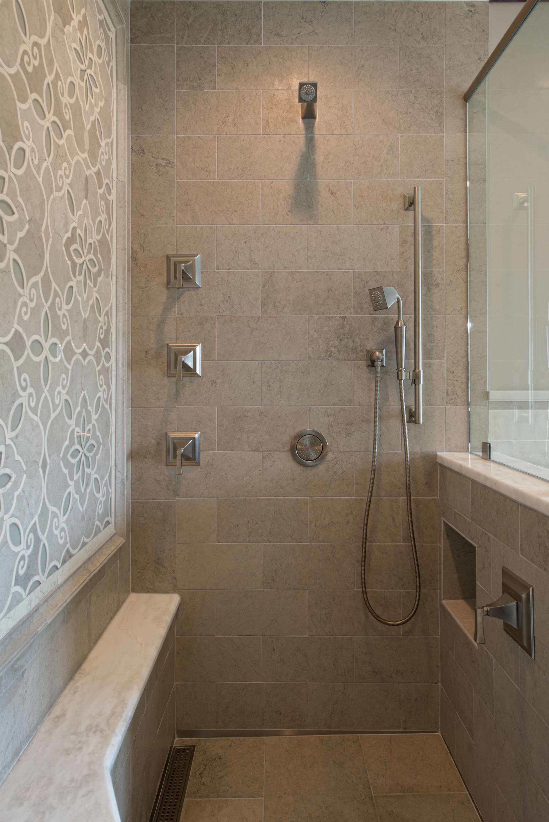Accessible tiled shower with grab bars, showerhead, bench, and handheld sprayer.