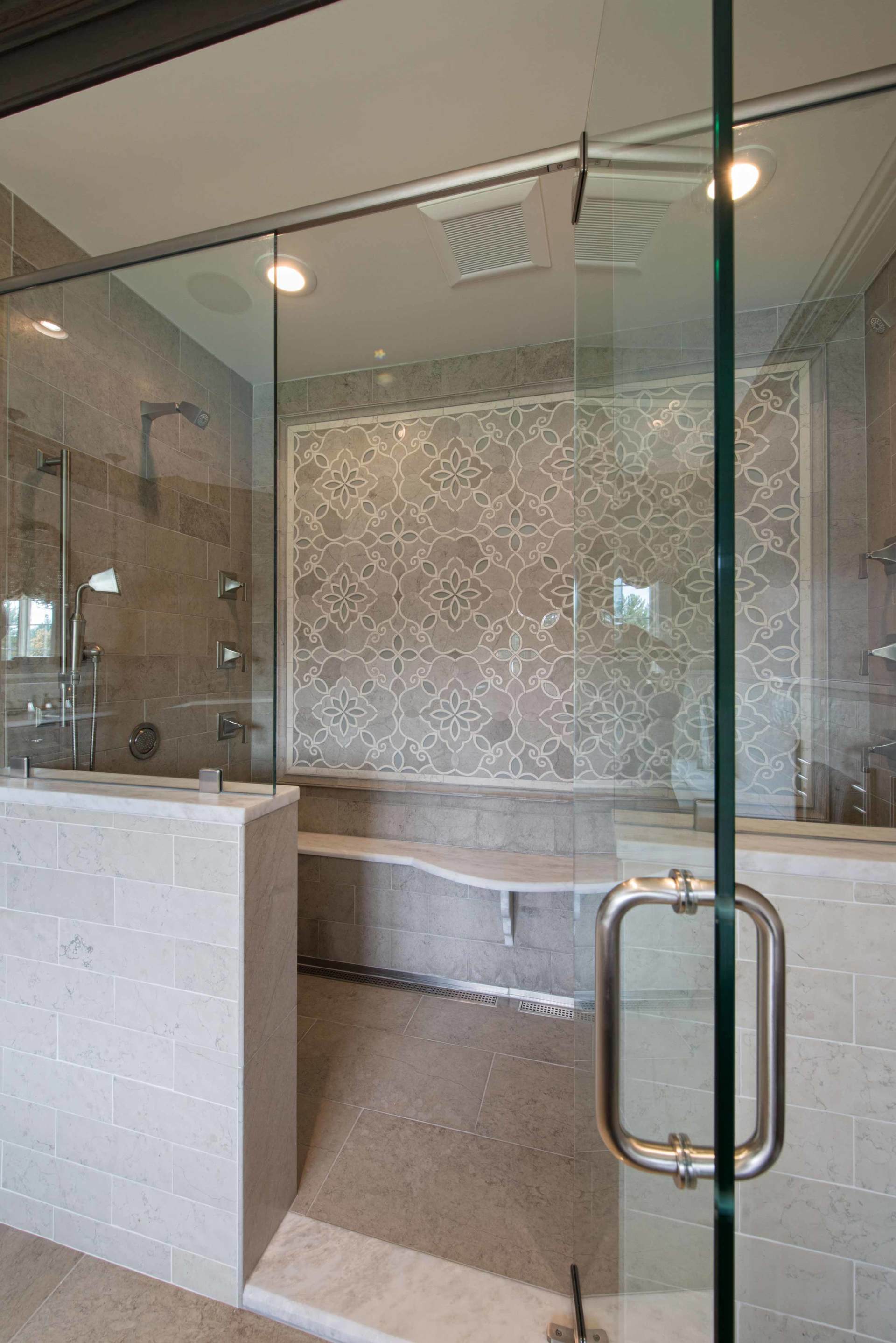 Modern glass shower enclosure with tiled walls, bench, and chrome door handle