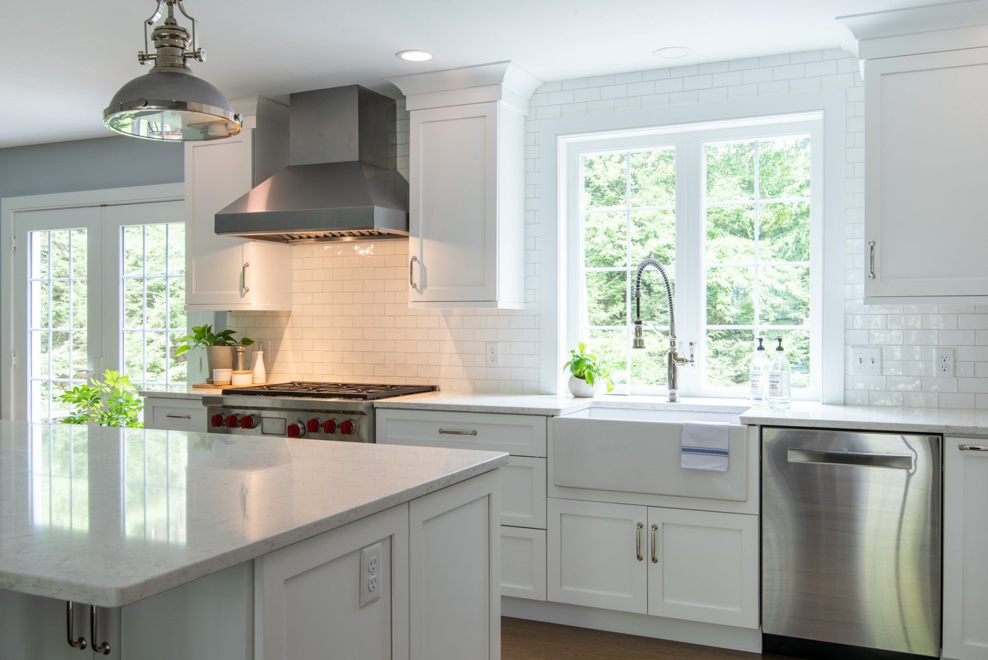 Bright white kitchen with marble island, stainless steel range hood, and large sunlit windows