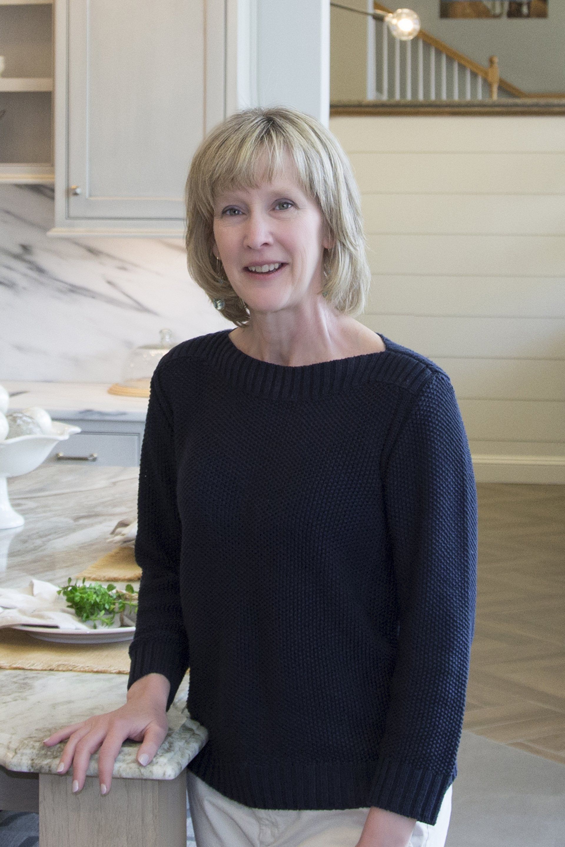 Woman in a black sweater standing in a bright kitchen by a marble countertop.