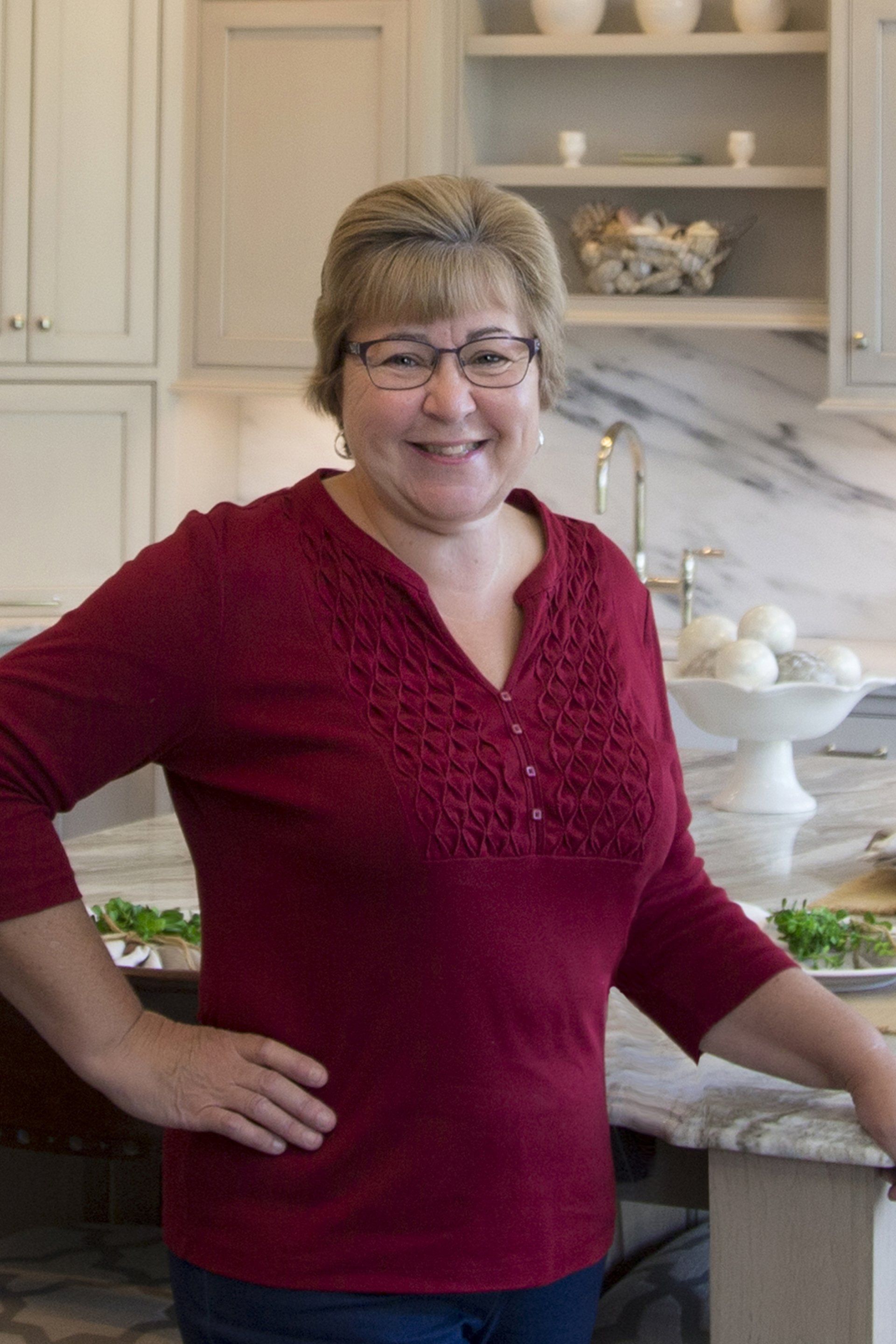 Woman in a red blouse smiling in a bright kitchen, leaning on a granite counter.