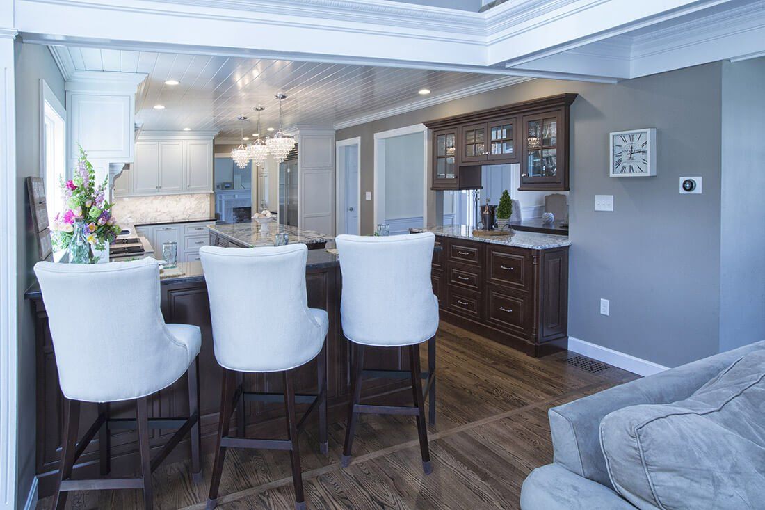 Modern kitchen and dining area with white bar stools, dark wood cabinets, and a gray sofa nearby