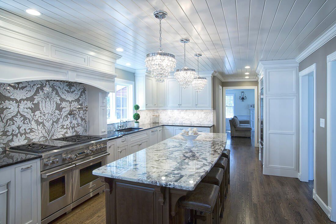 Bright modern kitchen with marble island, white cabinets, pendant lights, and dark wood flooring.