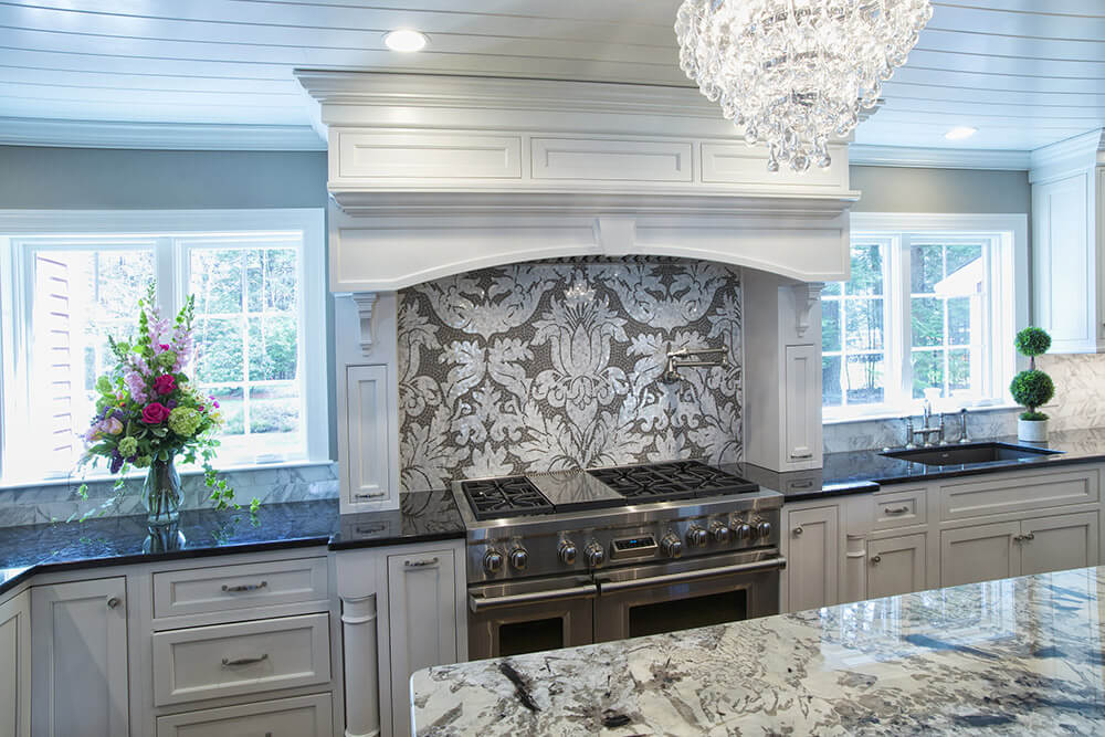 Luxurious kitchen with blue-gray cabinets, marble island, ornate backsplash, and chandelier