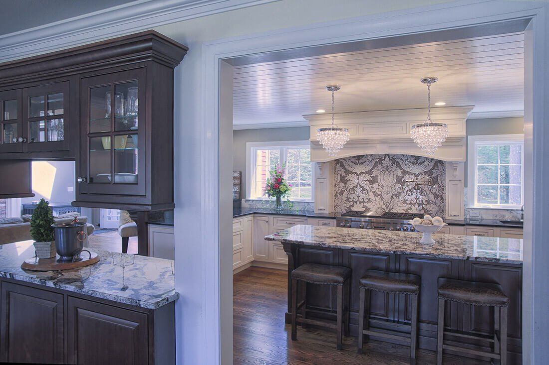 Open kitchen with dark cabinetry, stone island, and marble backsplash in a bright, elegant home