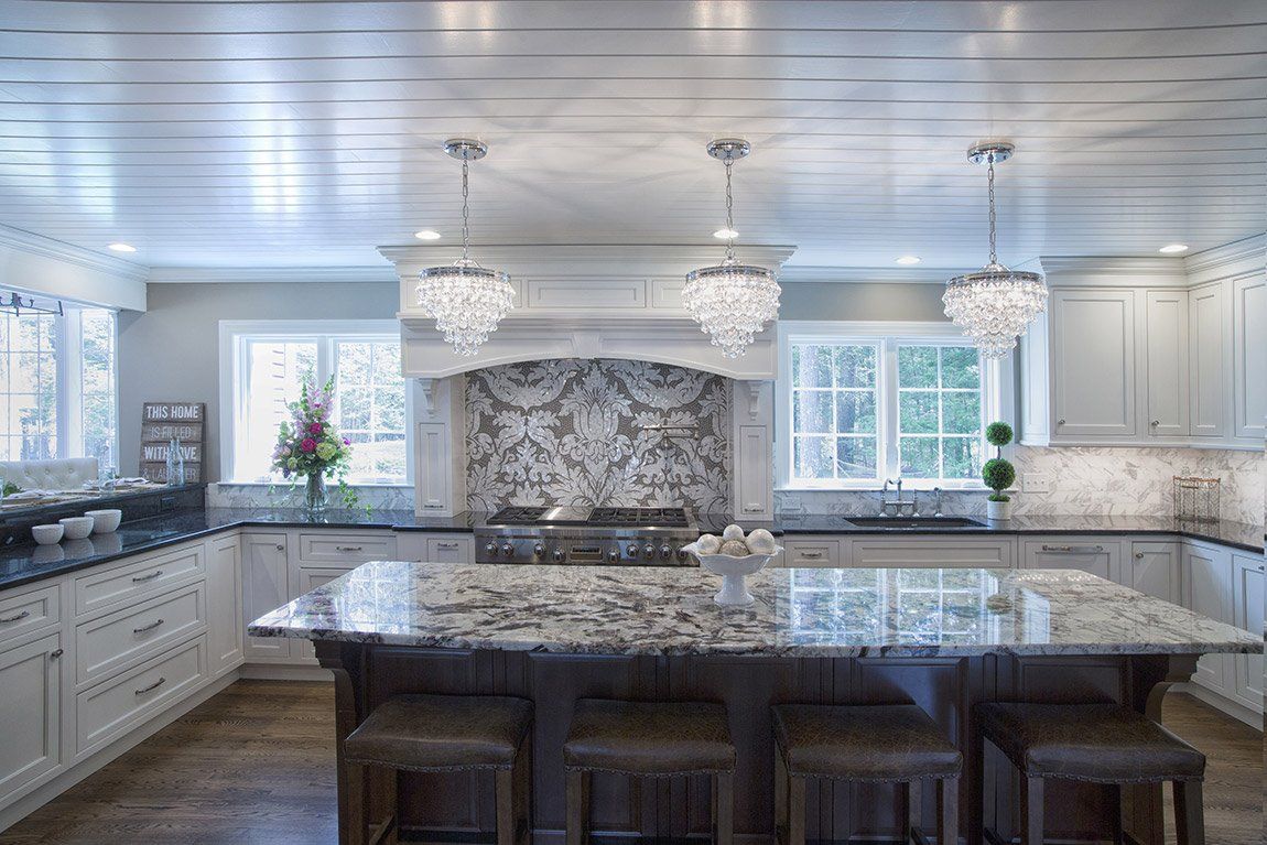 Bright modern kitchen with white cabinets, marble island, pendant lights, and stone backsplash