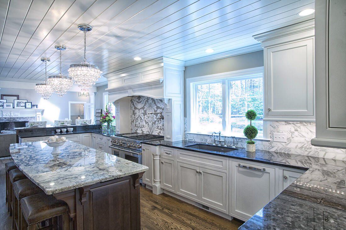 Bright modern kitchen with white cabinets, granite island, marble backsplash, and large window above the sink