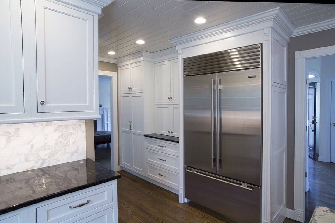 Bright white kitchen with stainless steel refrigerator, marble backsplash, and dark wood floor