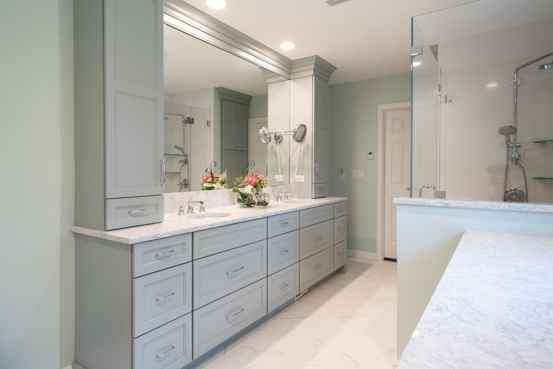 Bright modern bathroom with double vanity, large mirror, glass shower, and white marble countertops