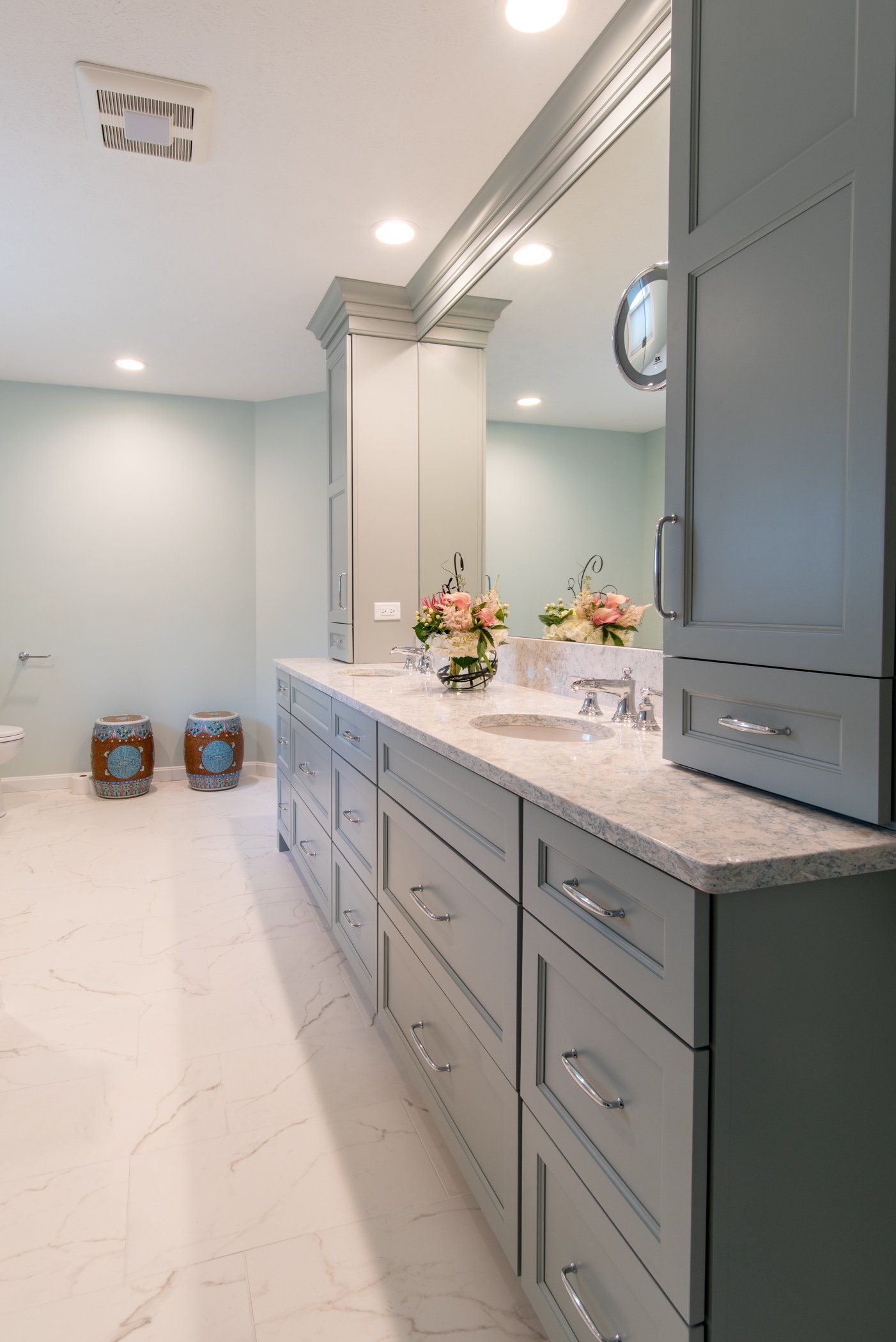 Elegant bathroom with gray cabinetry, white marble floor, large mirror, and floral accents