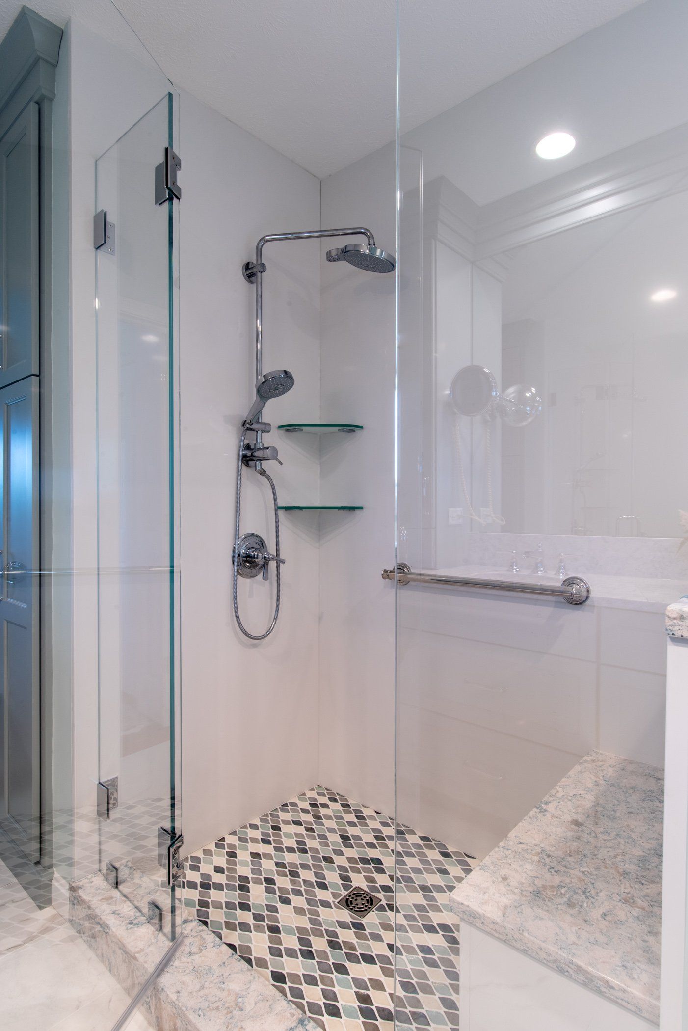 Modern white bathroom with glass shower, chrome fixtures, and pebble mosaic floor.