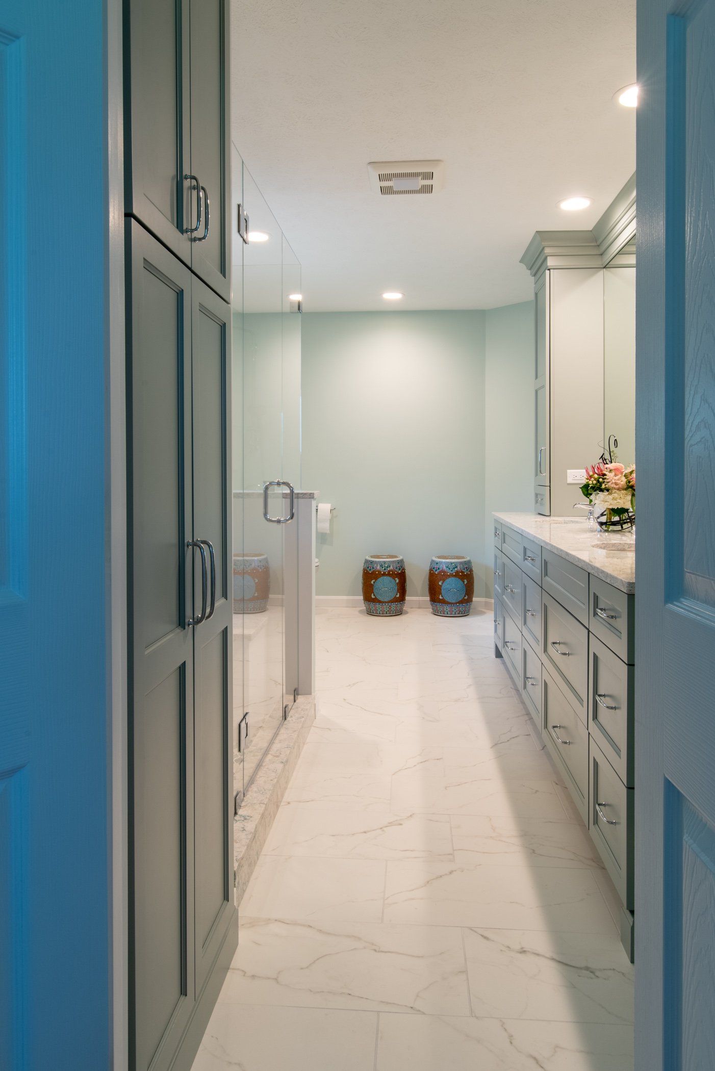 Narrow blue-and-white hallway with built-in cabinets, marble floor, and two decorative vases at the far end