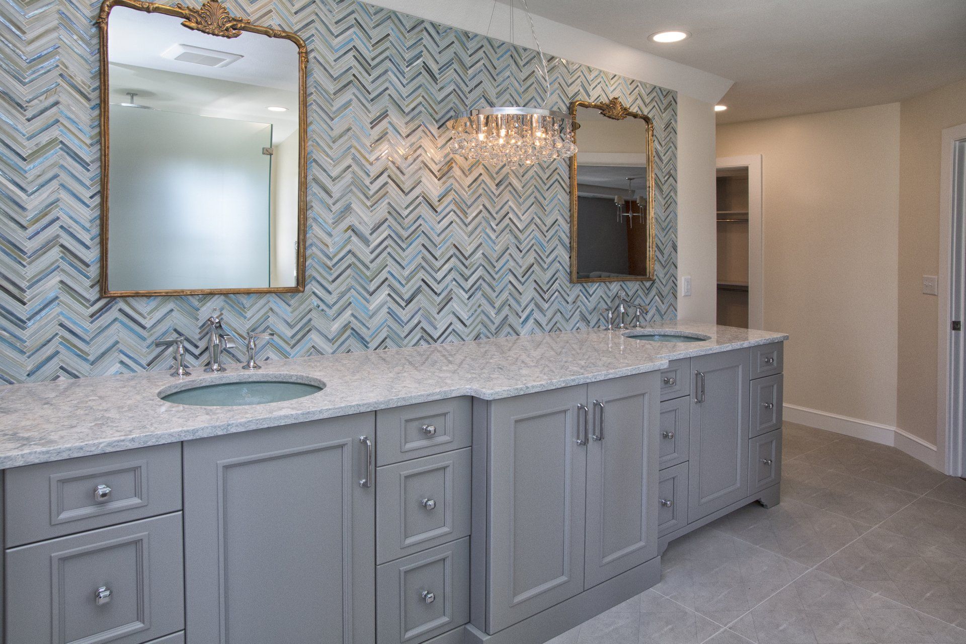 Modern bathroom with gray vanity, marble countertop, gold mirrors, and blue patterned tile backsplash