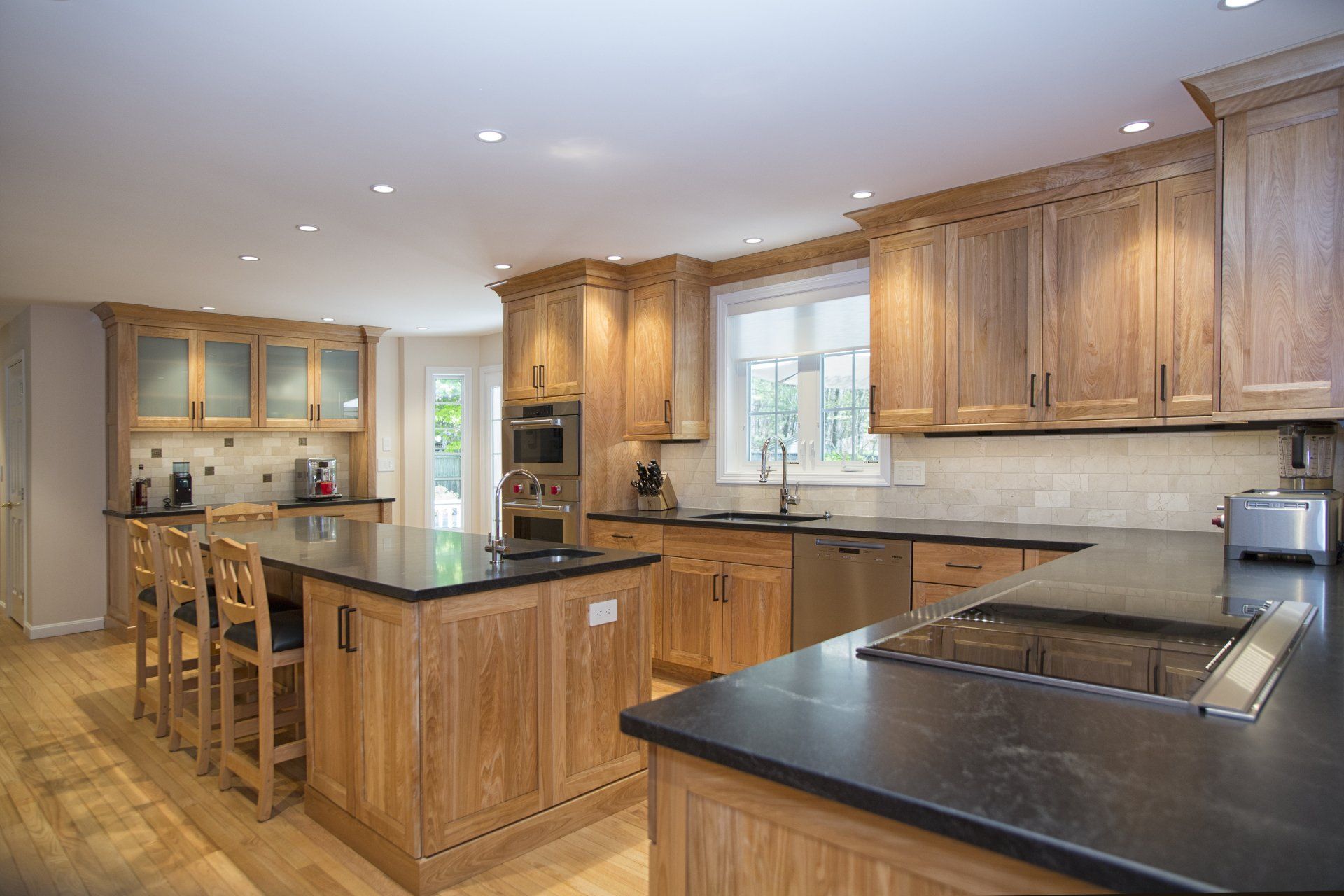 Spacious modern kitchen with wood cabinets, black countertops, island seating, and stainless steel appliances
