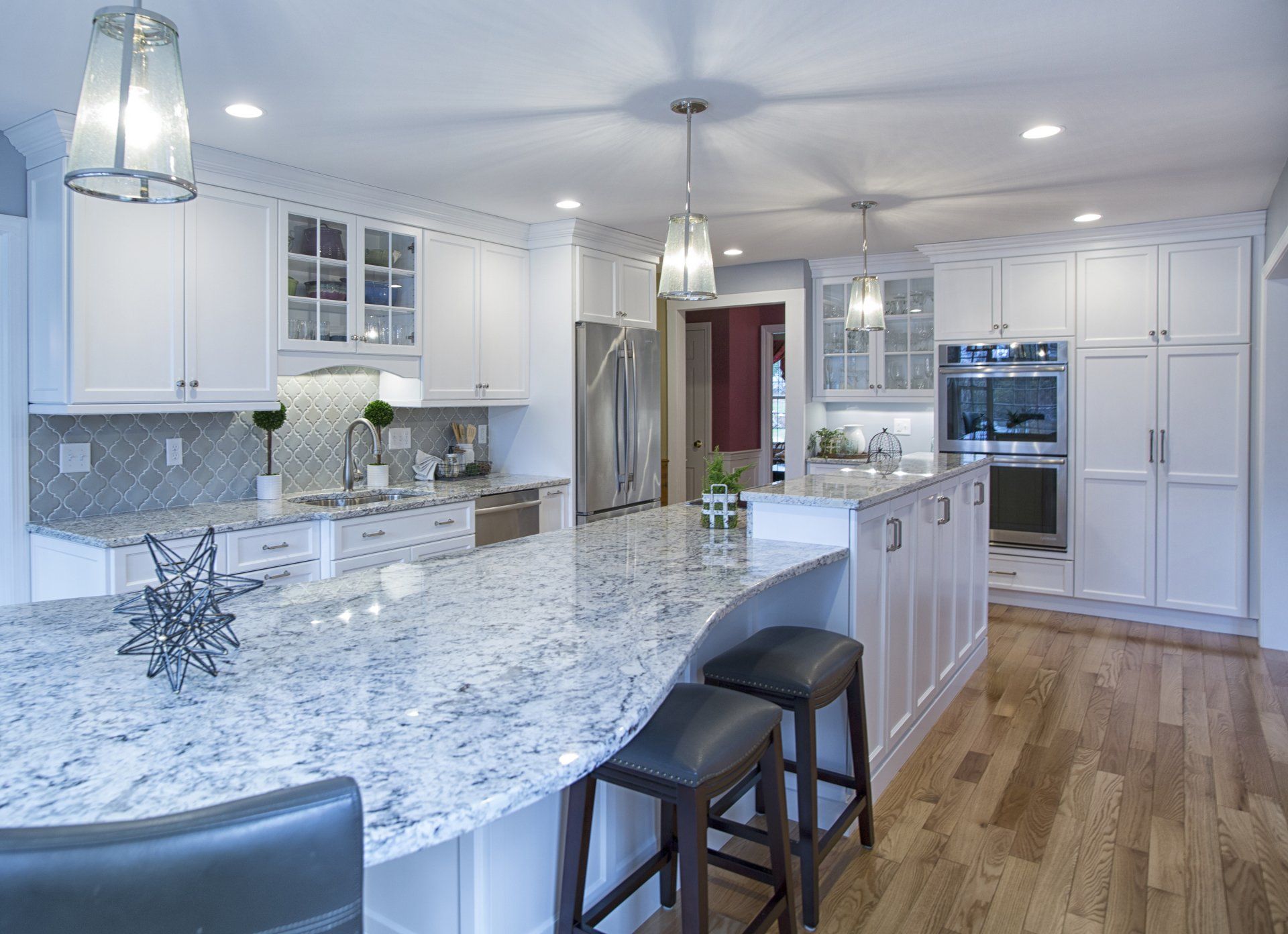 Bright modern kitchen with white cabinets, marble island, pendant lights, and hardwood floors