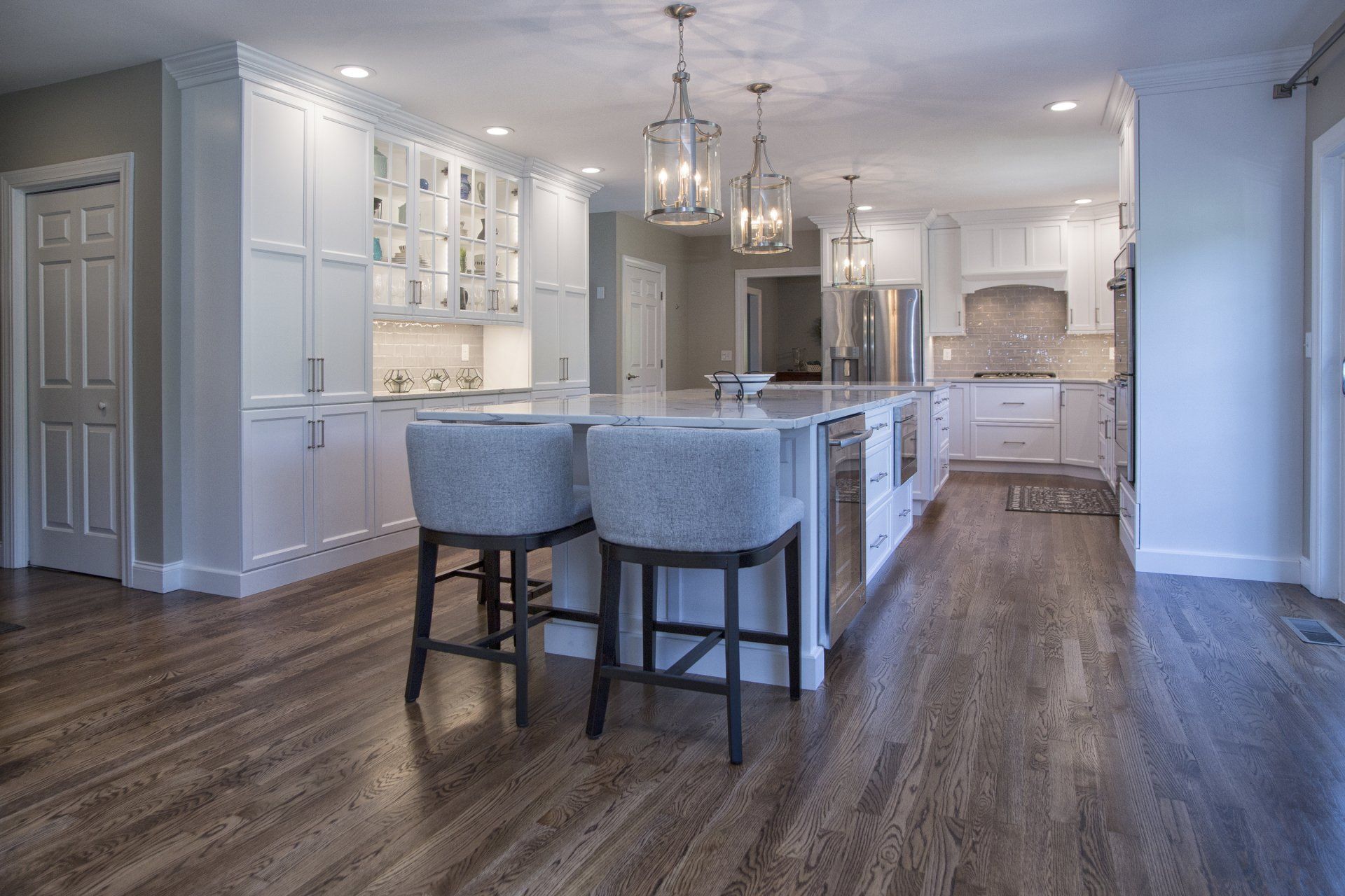 Bright modern kitchen with white cabinets, gray island, pendant lights, and two upholstered stools
