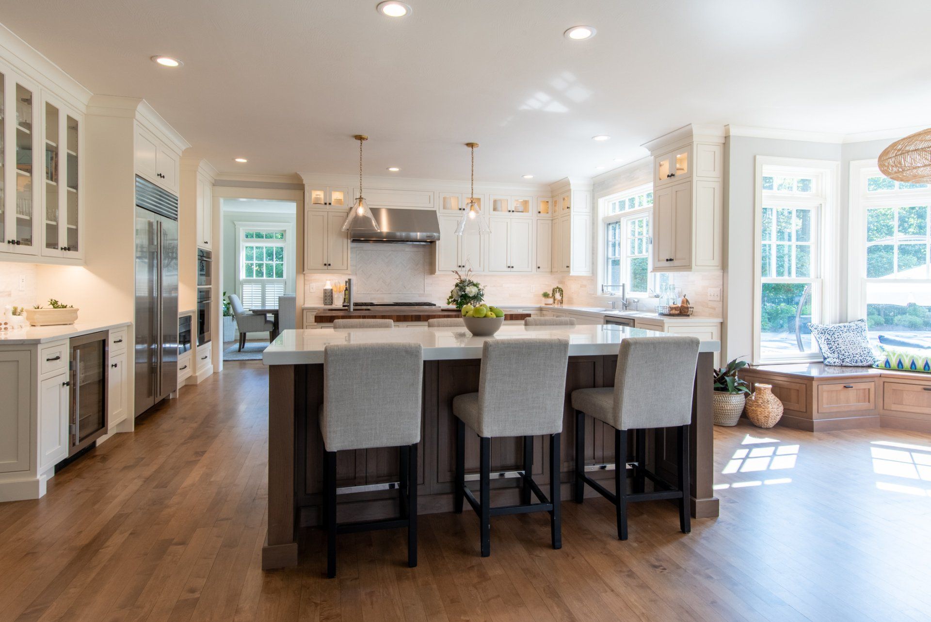 Bright open kitchen with large island, white cabinets, hardwood floors, and a sunlit bay window seating area