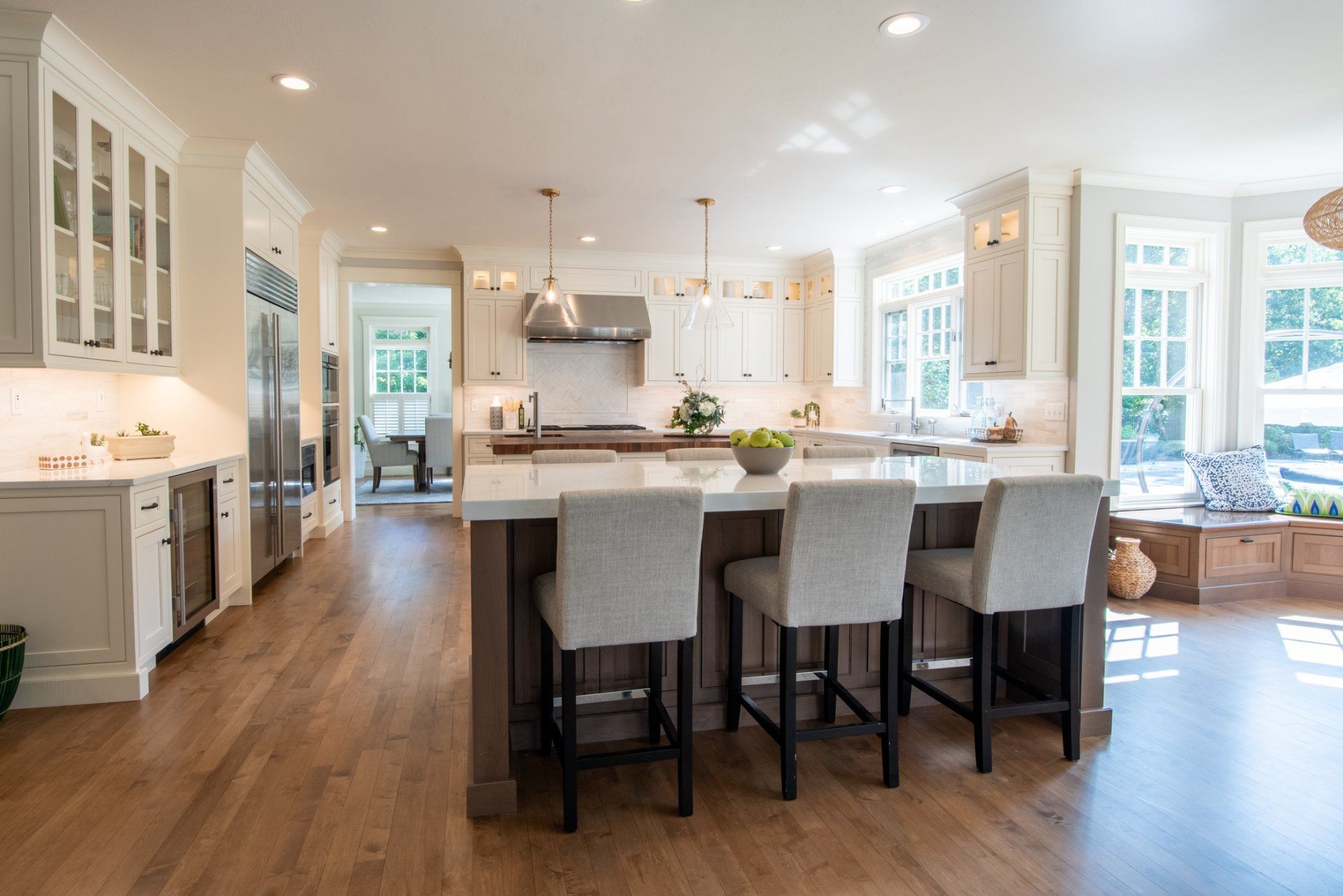 Bright modern kitchen with white cabinets, wood floors, large island, and bar stools