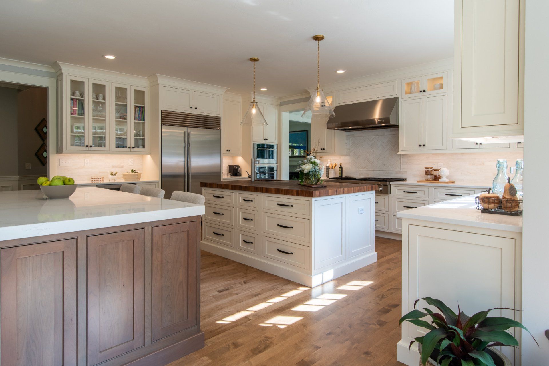 Bright modern kitchen with white cabinets, marble island, stainless fridge, and sunlight on wood floor