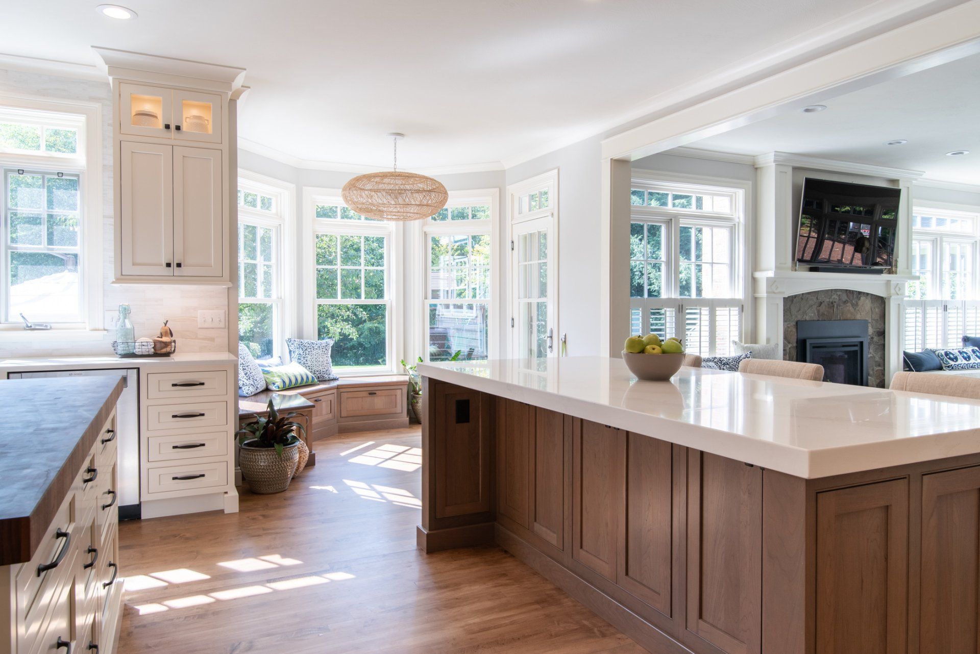 Bright white kitchen with a large island, wood floors, and sunlit bay windows.