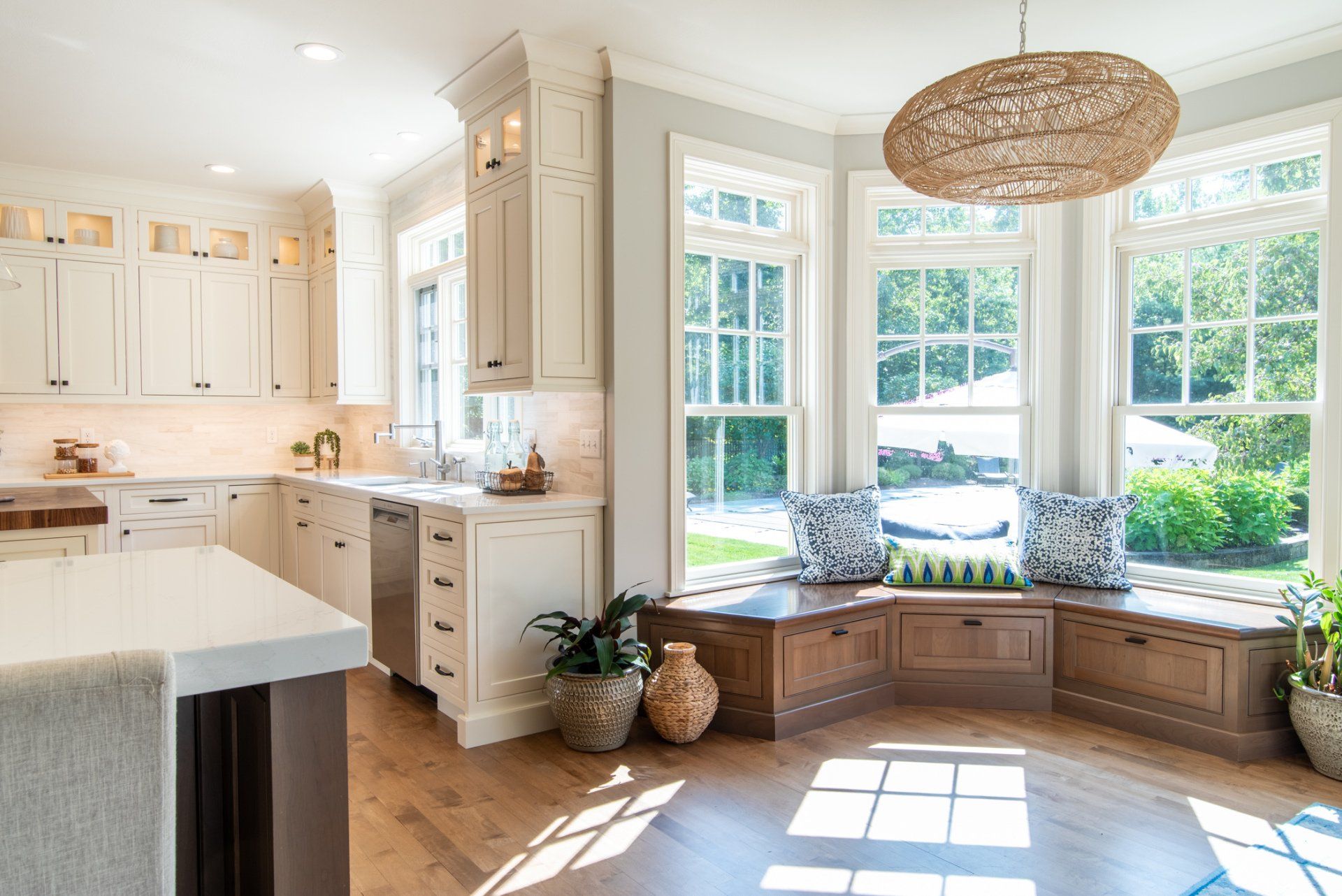 Bright white kitchen with bay window bench, woven chandelier, and sunlit floor.