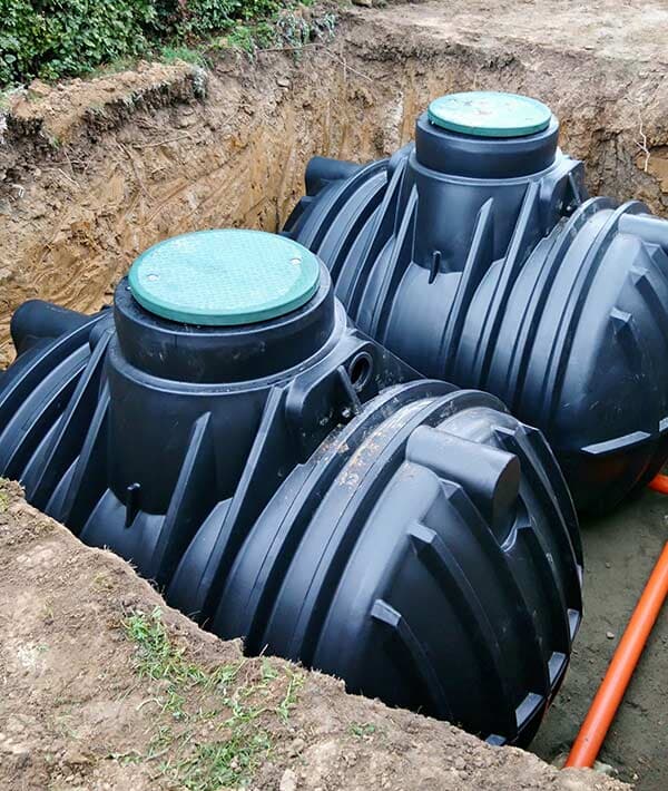 Two Large Black Septic Tanks With Green Lids Are Installed in a Freshly Dug Trench