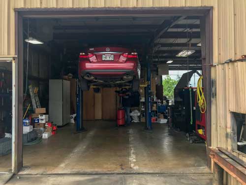 A red car is sitting on a lift in a garage.