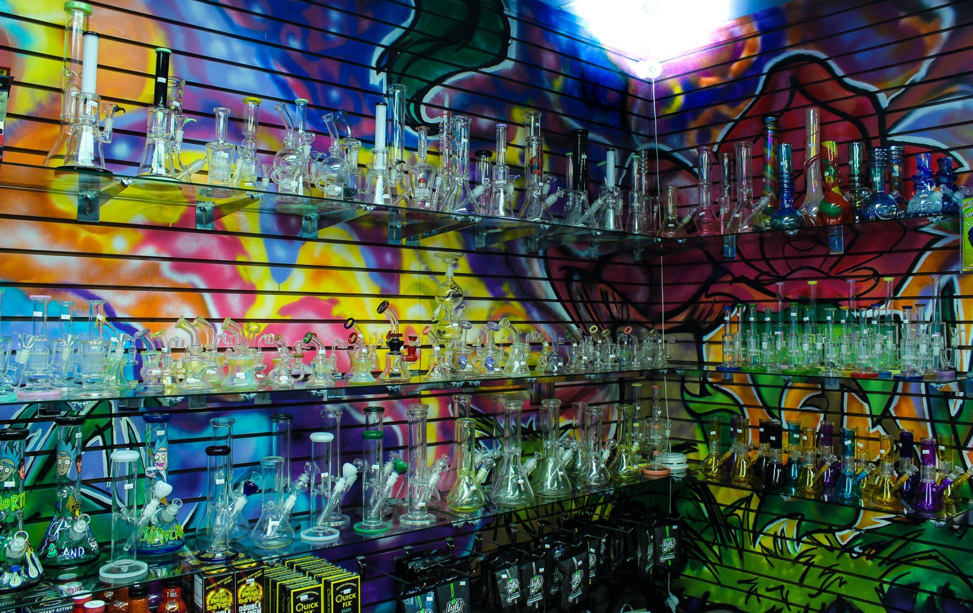 A display of glass pipes and bongs in front of a colorful wall.