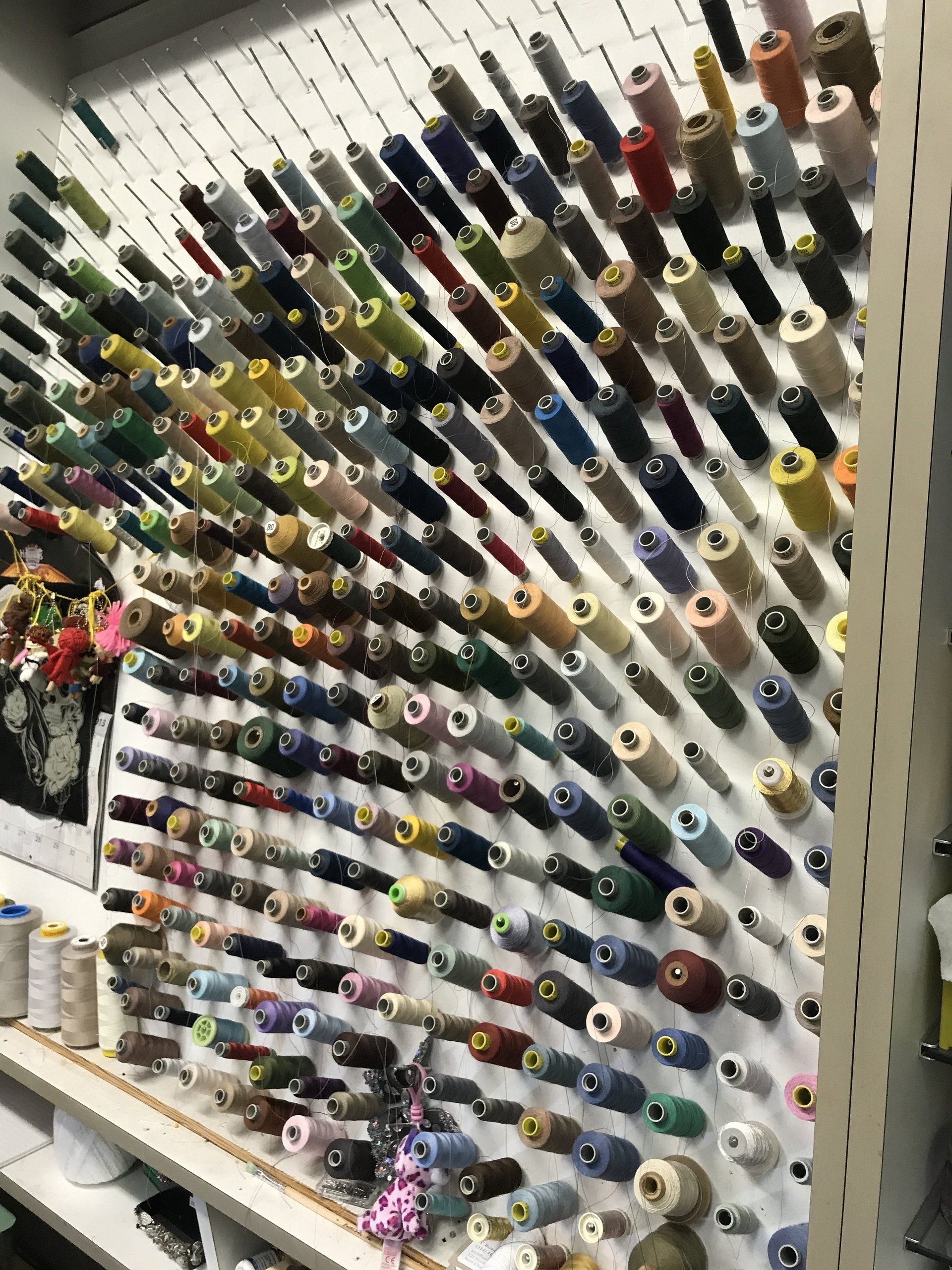 Wall display of colorful thread spools arranged in neat rows on angled shelves.