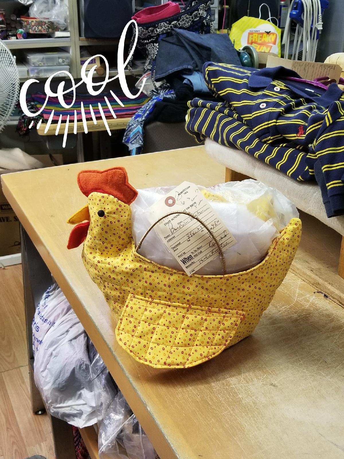 Yellow woven chicken basket filled with white cloth on a wooden table, with folded clothes in the background